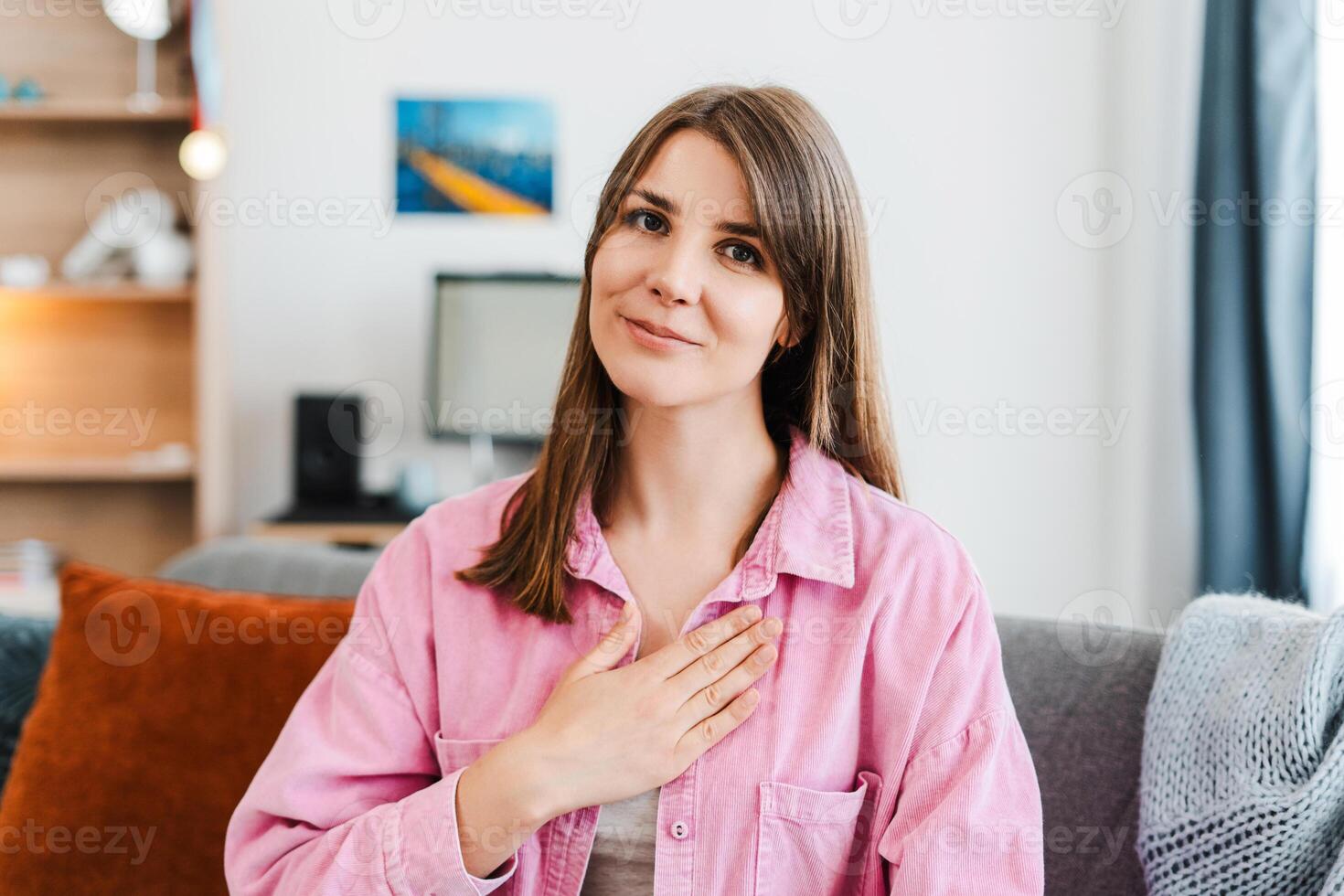 Beautiful, grateful woman, looking at camera, sitting on comfortable sofa at home photo