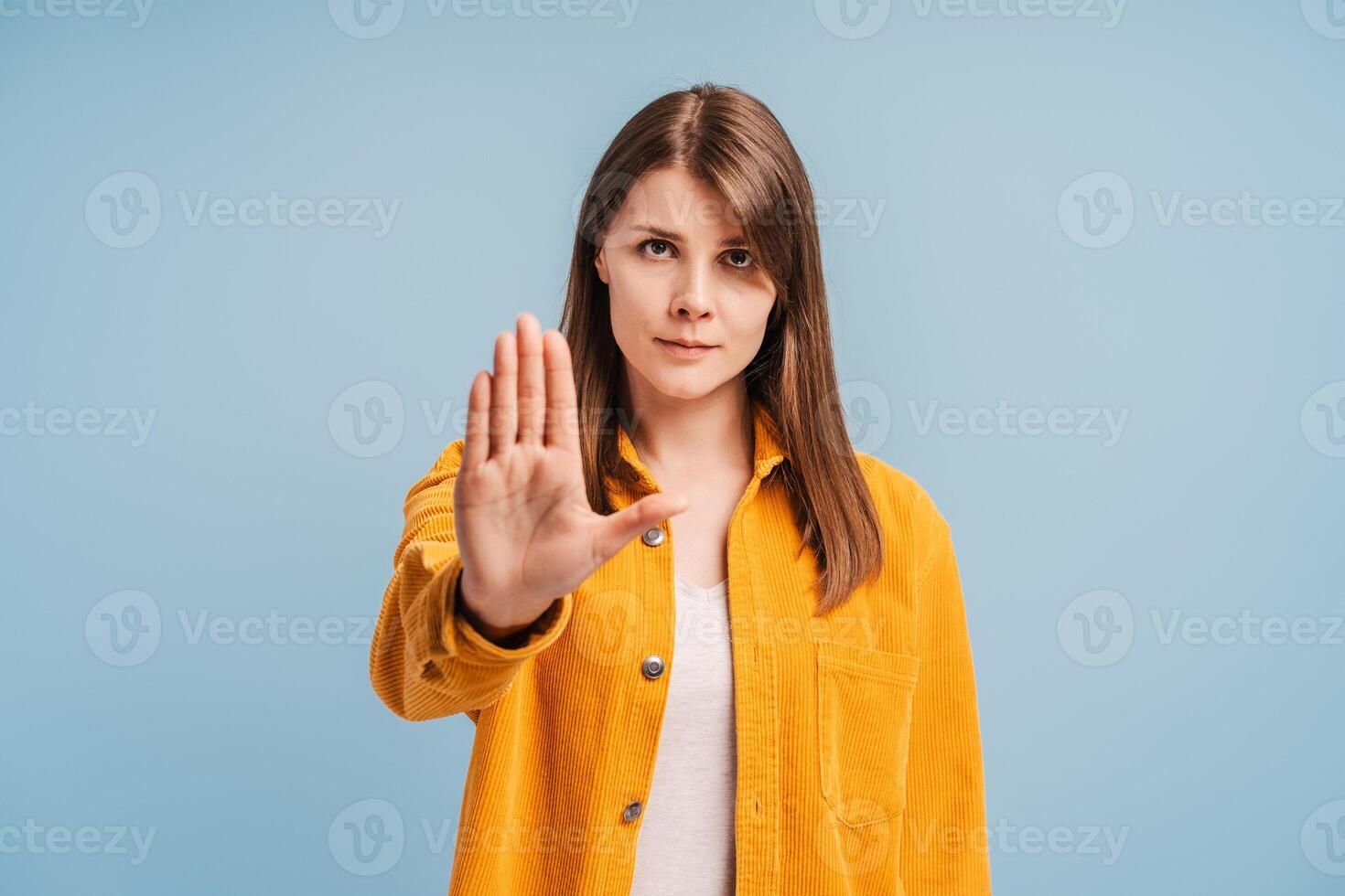 Serious attractive woman wearing stylish yellow shirt showing stop sign, looking at camera photo