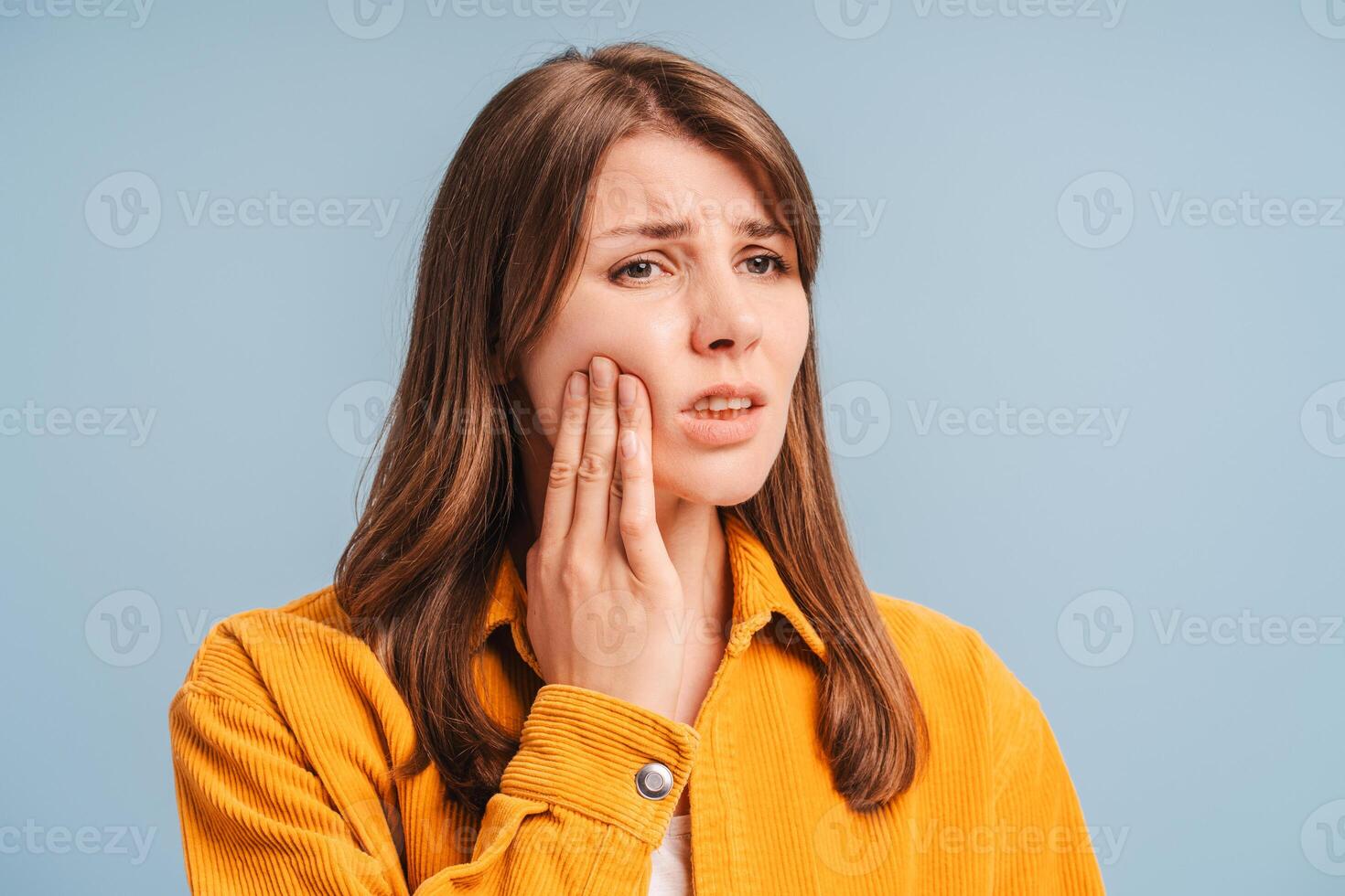 Sad woman touching cheek, having toothache isolated on blue background. Female patient looking away photo