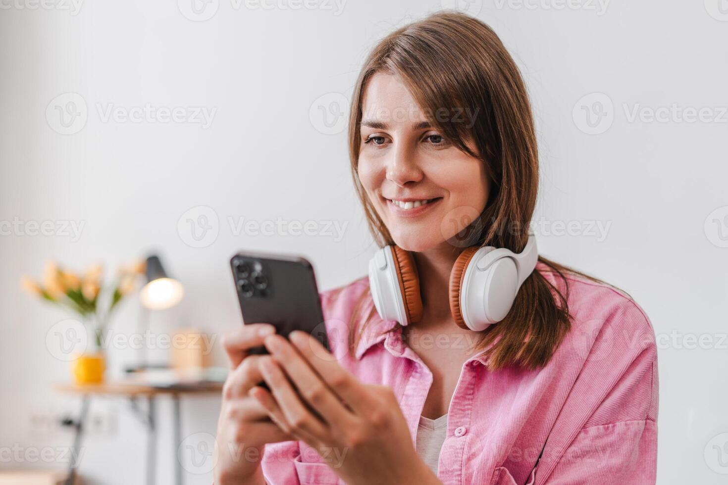 Smiling, attractive woman listening music in earphones, using mobile phone, text message photo