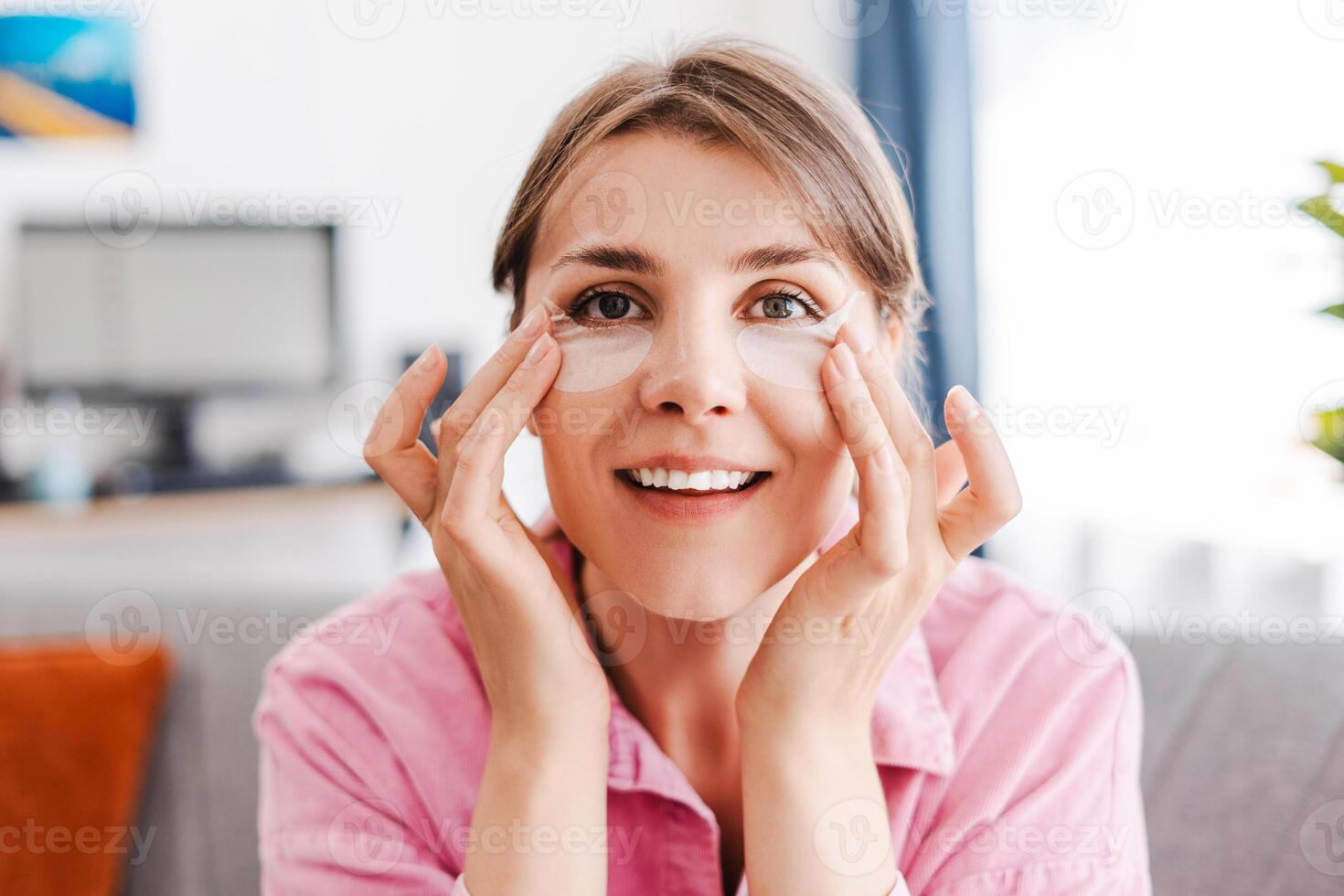 Beautiful, smiling woman with under eye patches on her face, moisturizing, looking at camera photo
