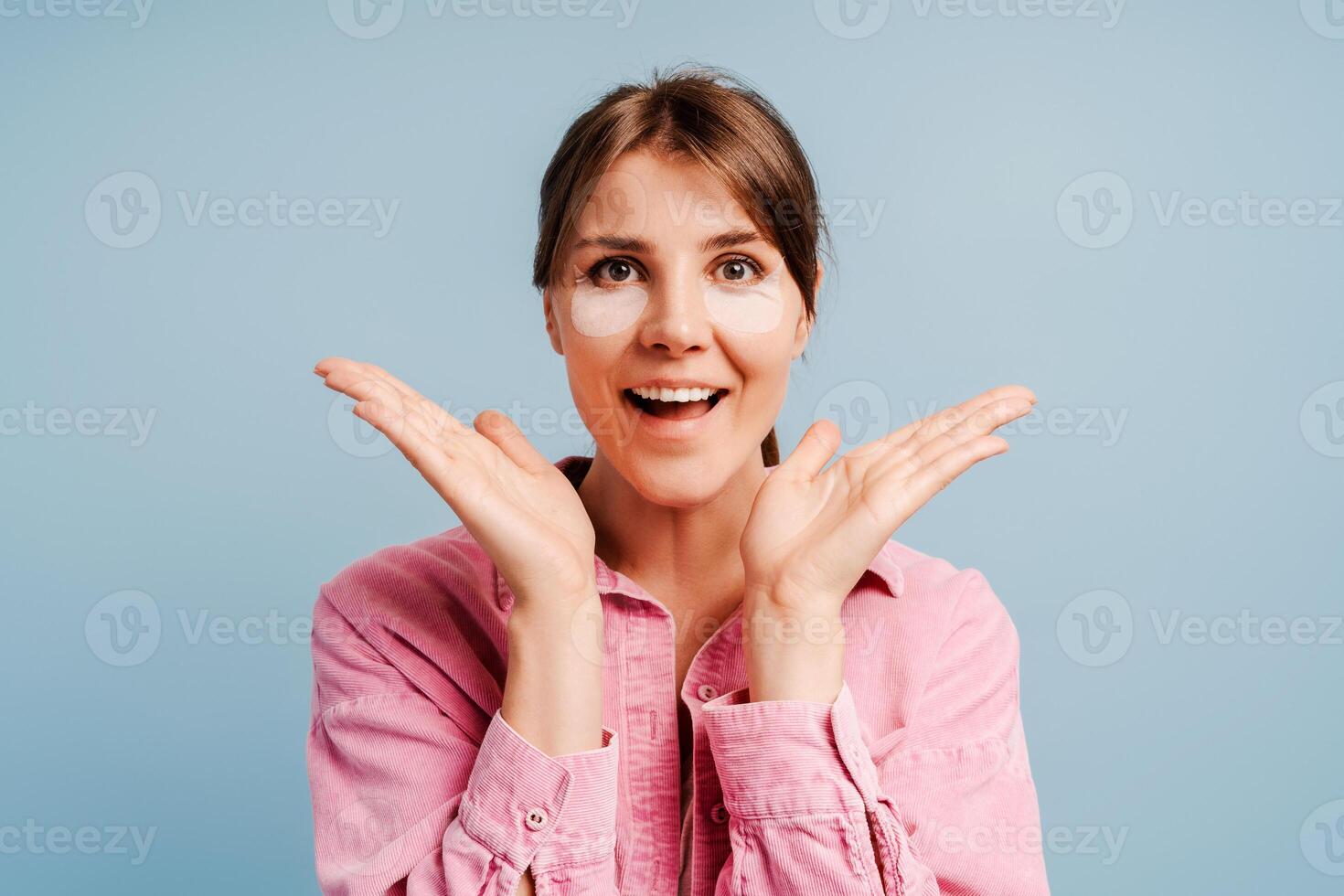 Excited beautiful woman with patches under eyes looking at camera posing isolated on blue background photo