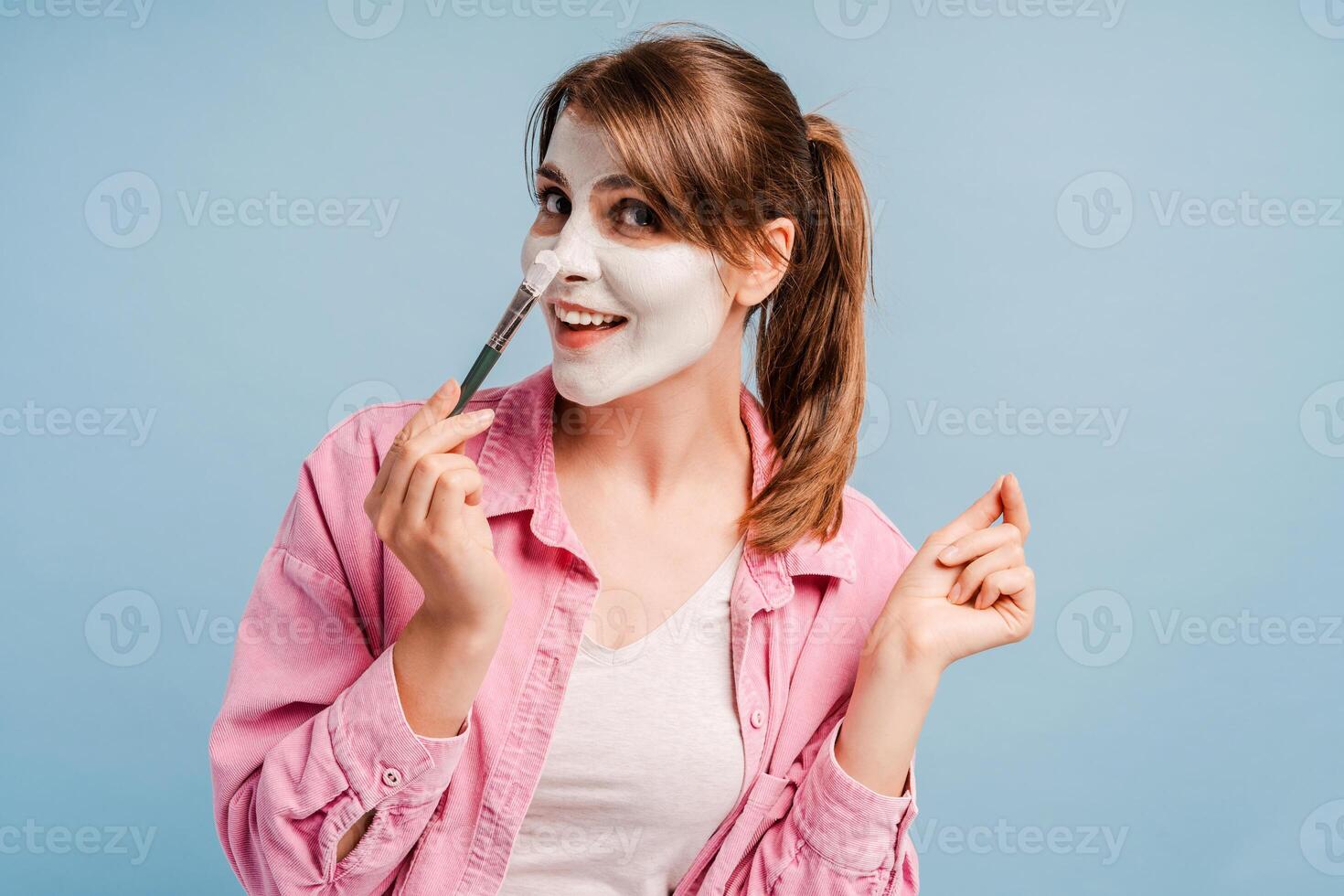 Smiling happy woman holding cosmetic brush, applying cosmetic mask, looking at camera photo