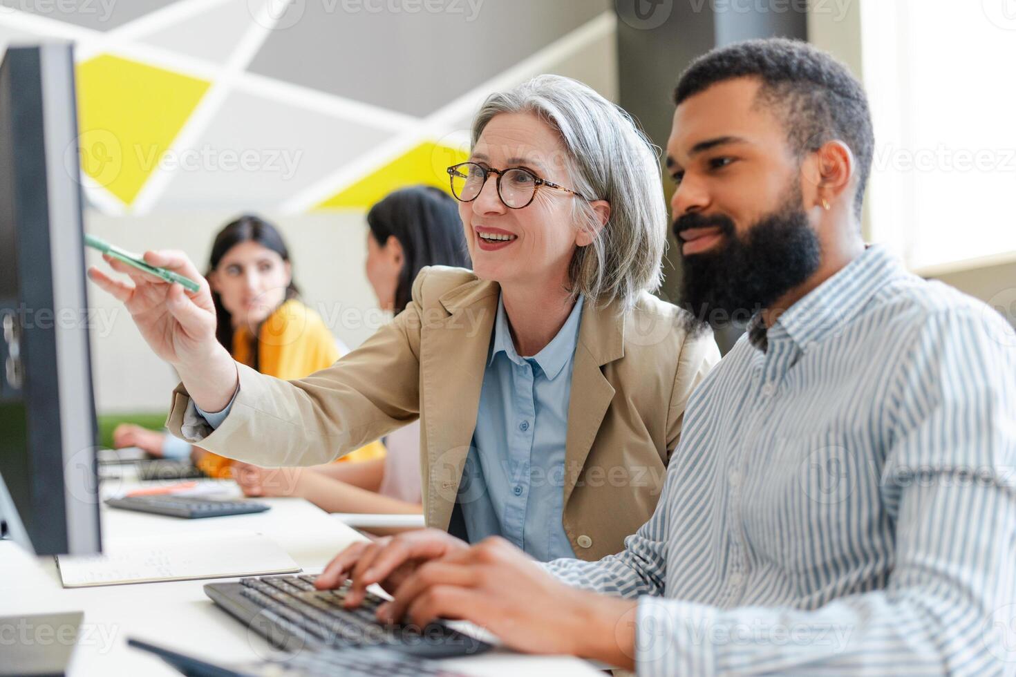 Senior female manager helping young developer working on desktop computer photo