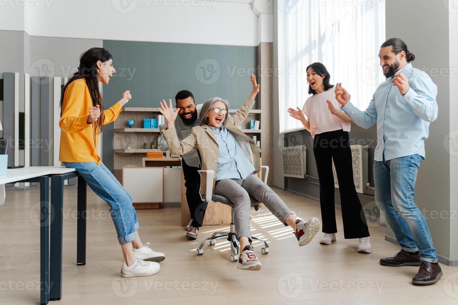 Diverse, multinational team celebrating success pushing colleague on office chair photo