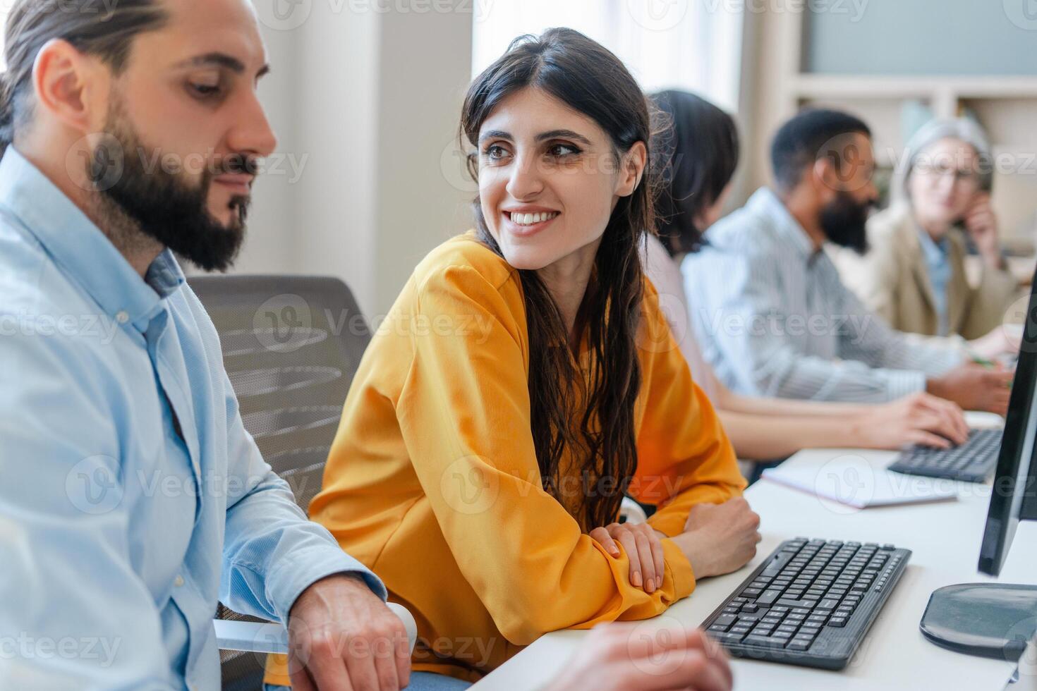 Young businesswoman smiling at colleague while working on computer in busy office photo