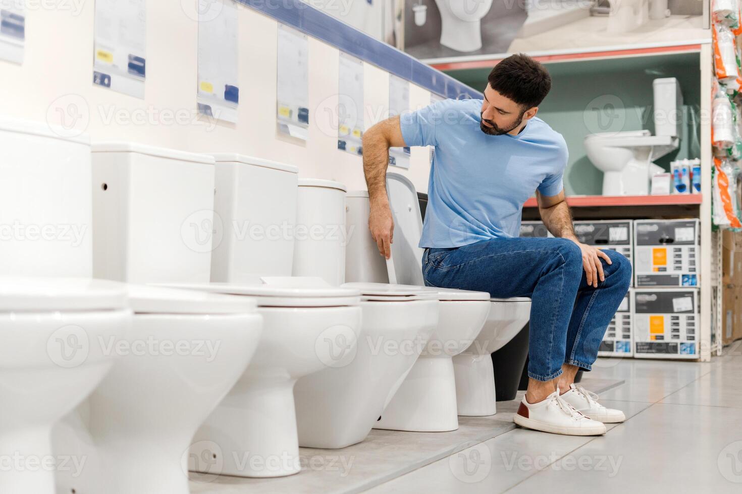Young man sitting and choosing new toilet in hardware store, checking the quality photo