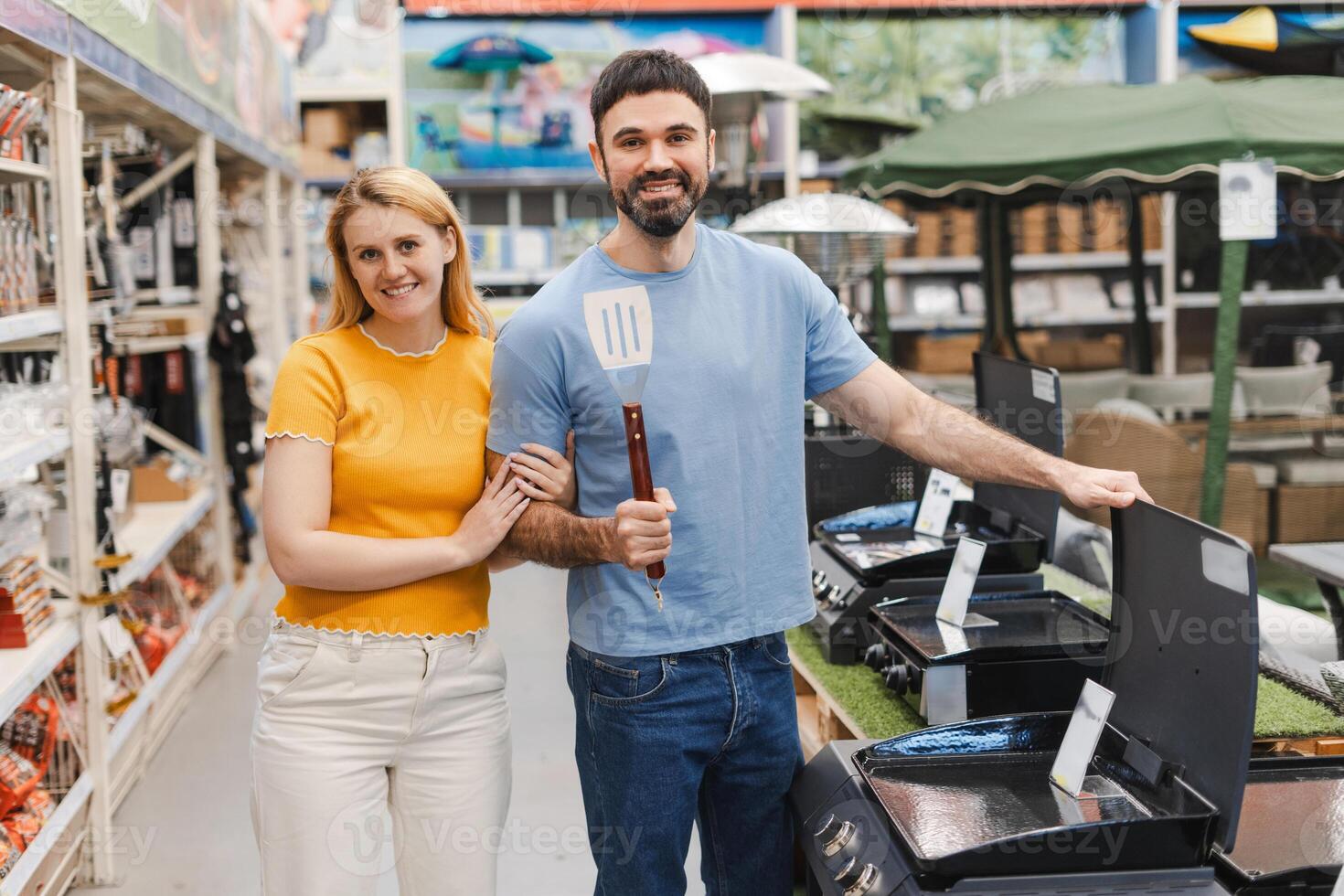 Happy married couple inspecting mobile grill, buying barbecue appliance in store photo