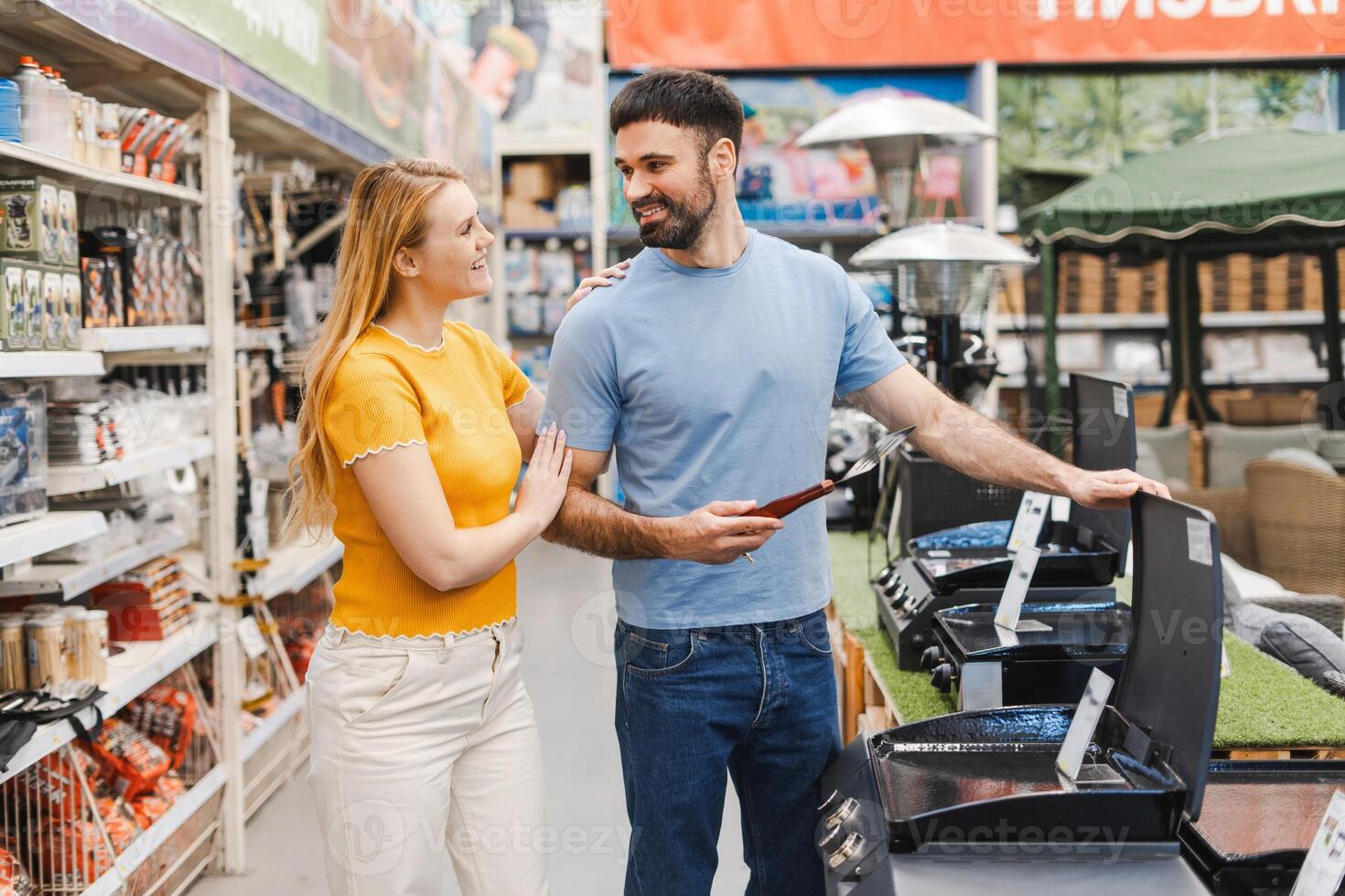 Happy young couple choosing barbeque at electric store while looking each other photo