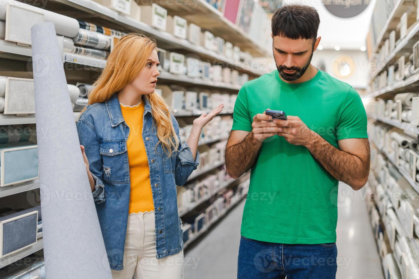 Young man typing on the mobile phone while woman holding wallpapers in construction store photo