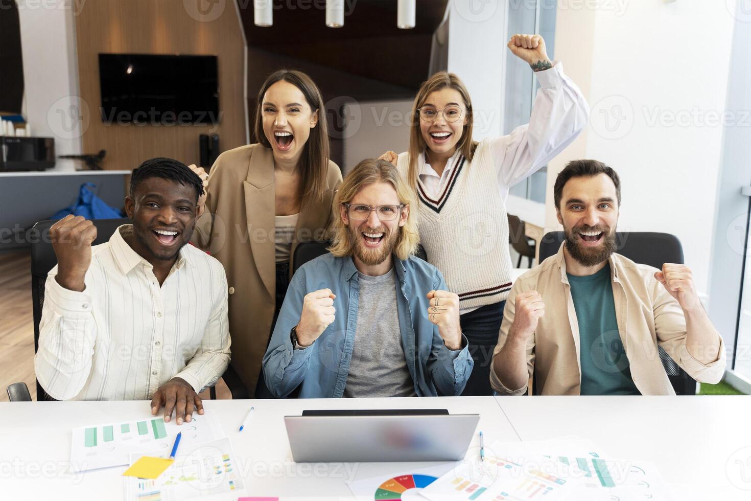 Excited business team celebrating success around laptop in modern office photo