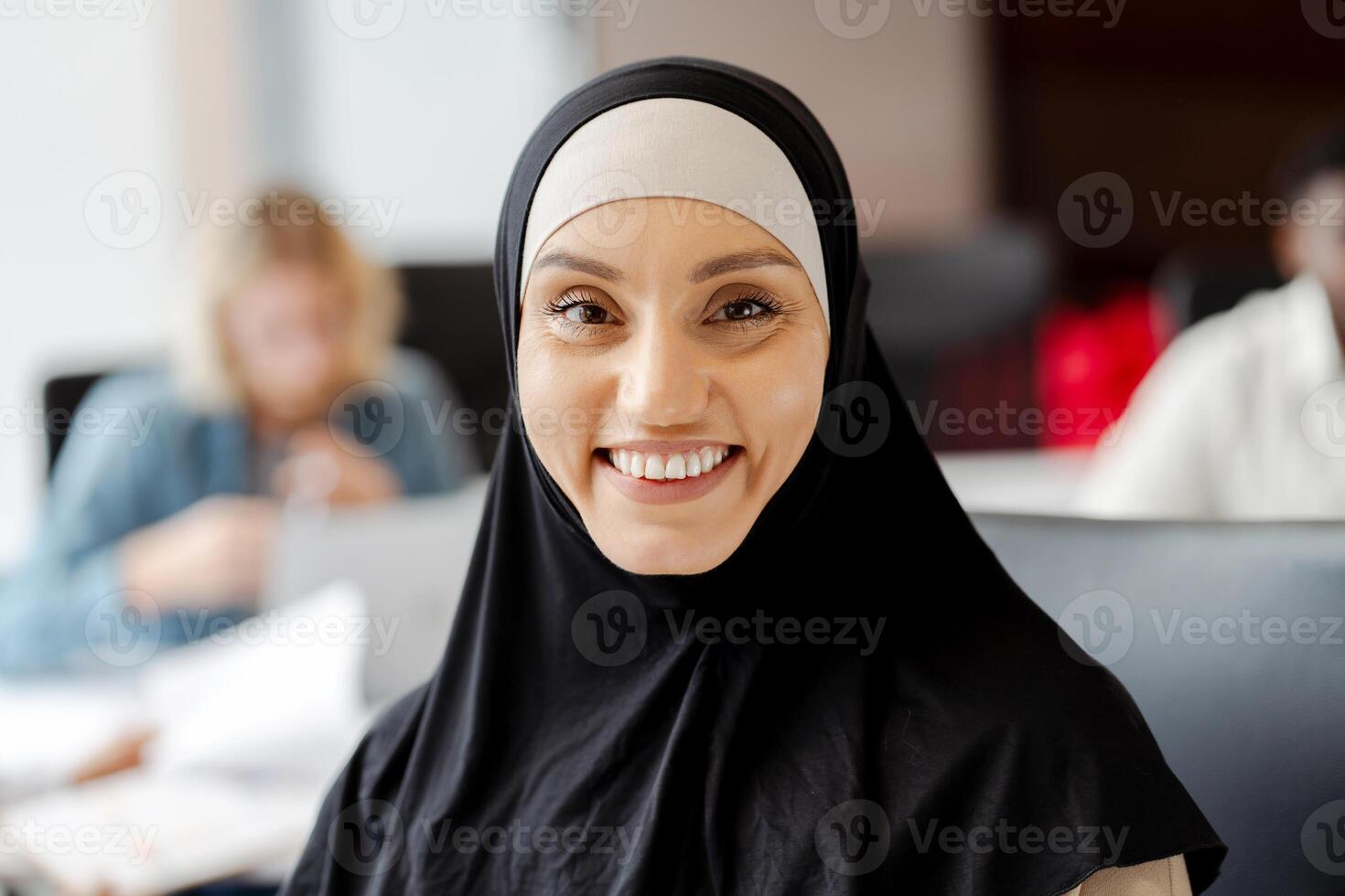 Young muslim woman smiling while working in busy office looking at camera photo