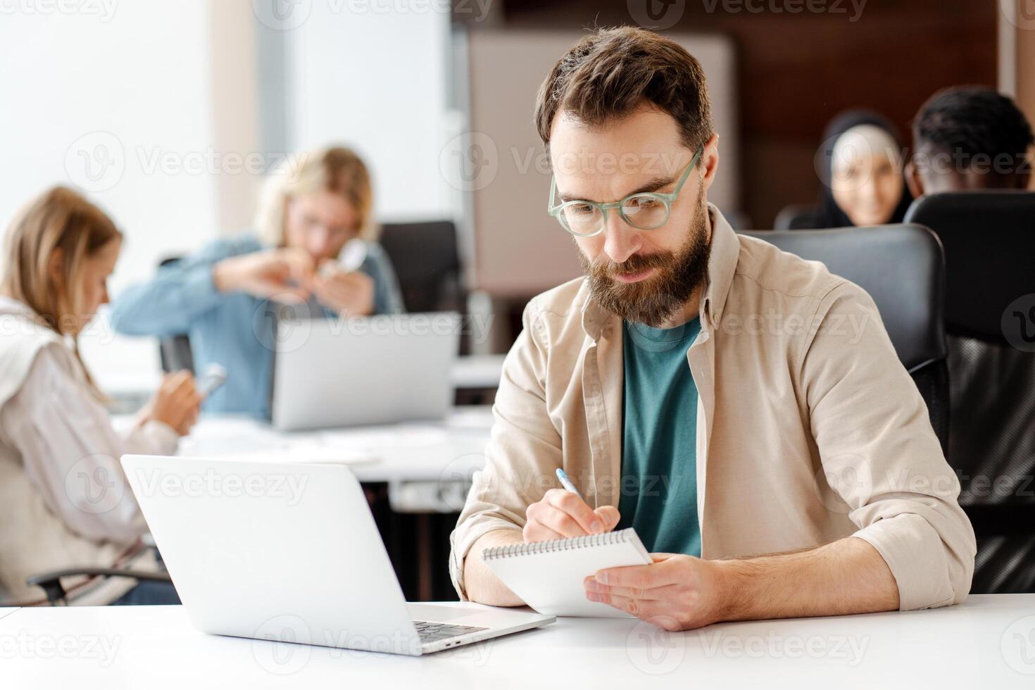 Focused male, manager, office worker taking notes during meeting, using laptop photo