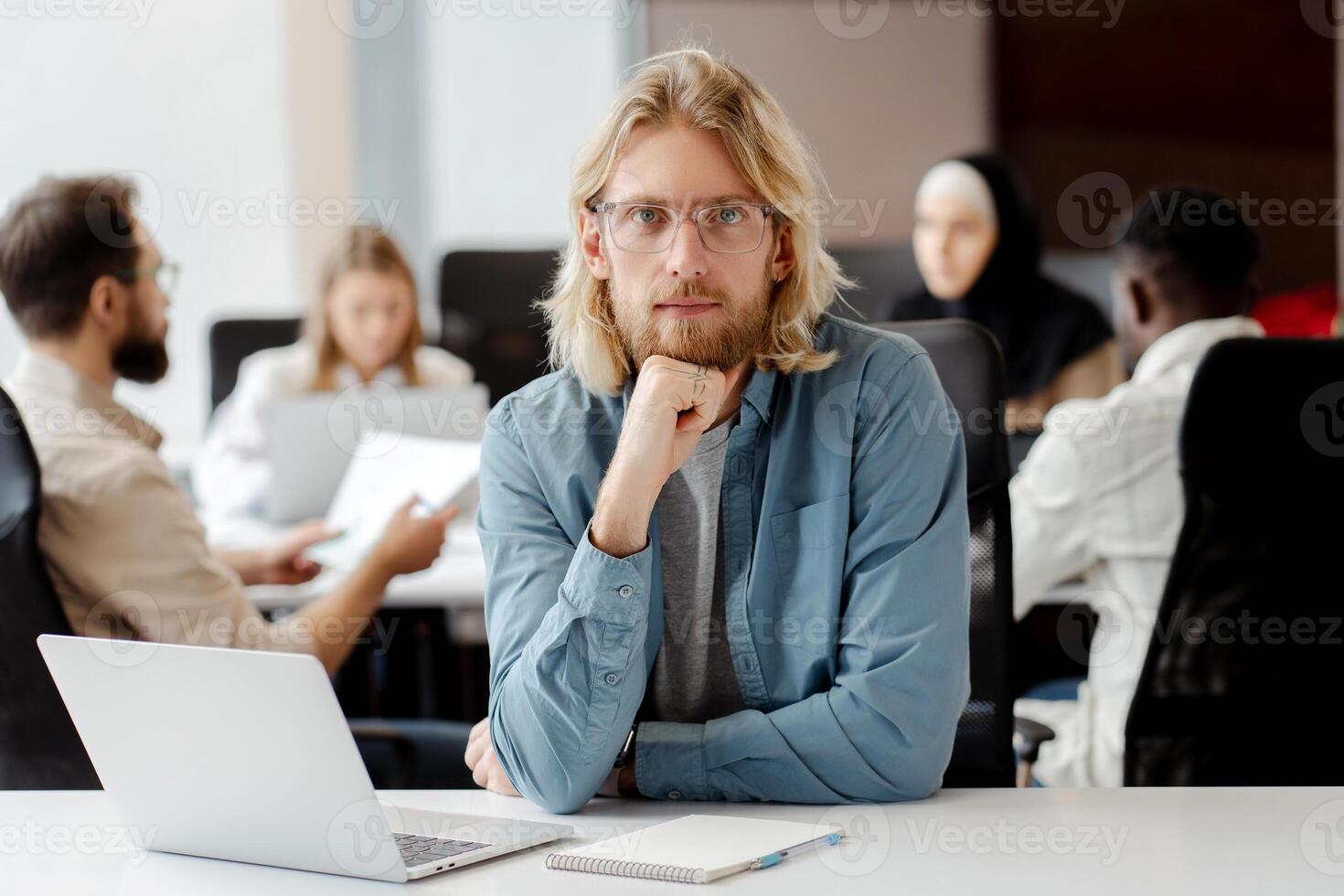 Handsome project manager sitting at desk with team working in background photo