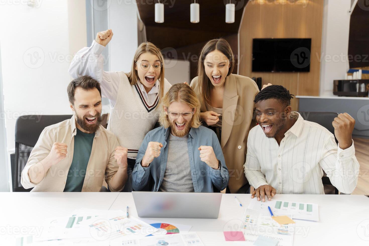 Excited diverse business team celebrating success looking at laptop in office photo