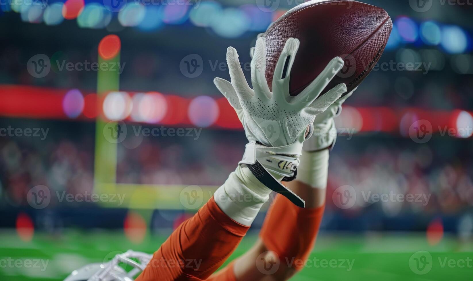 A football player's hands catching the ball mid-air, with the field and goalposts in the background photo