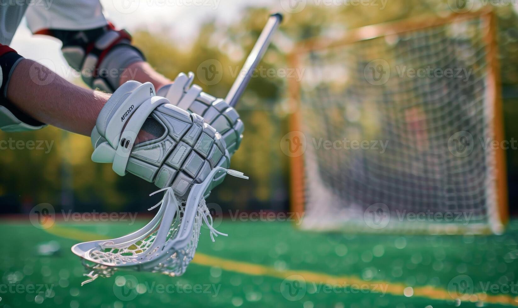 A lacrosse player's hands holding a stick, with the field and net in the background photo