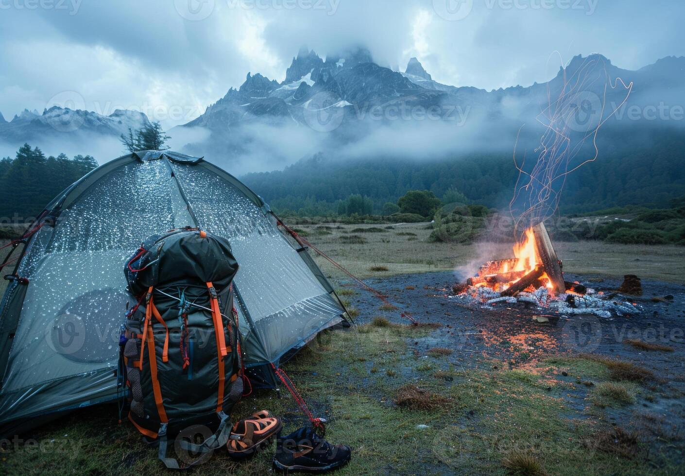 A tent and backpack are set up near a campfire photo