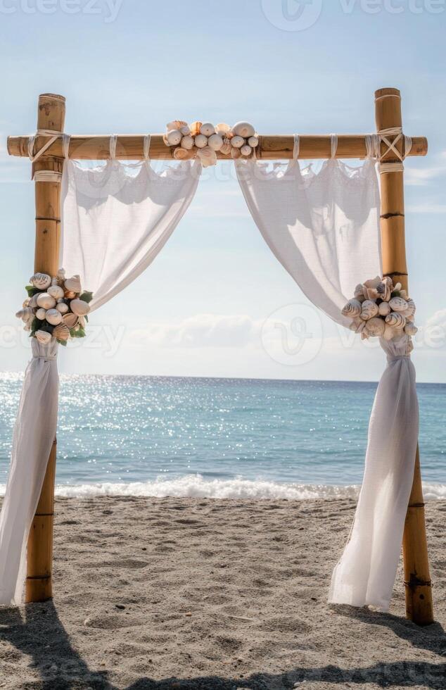 A bamboo arch with white drapes and shells on the beach photo