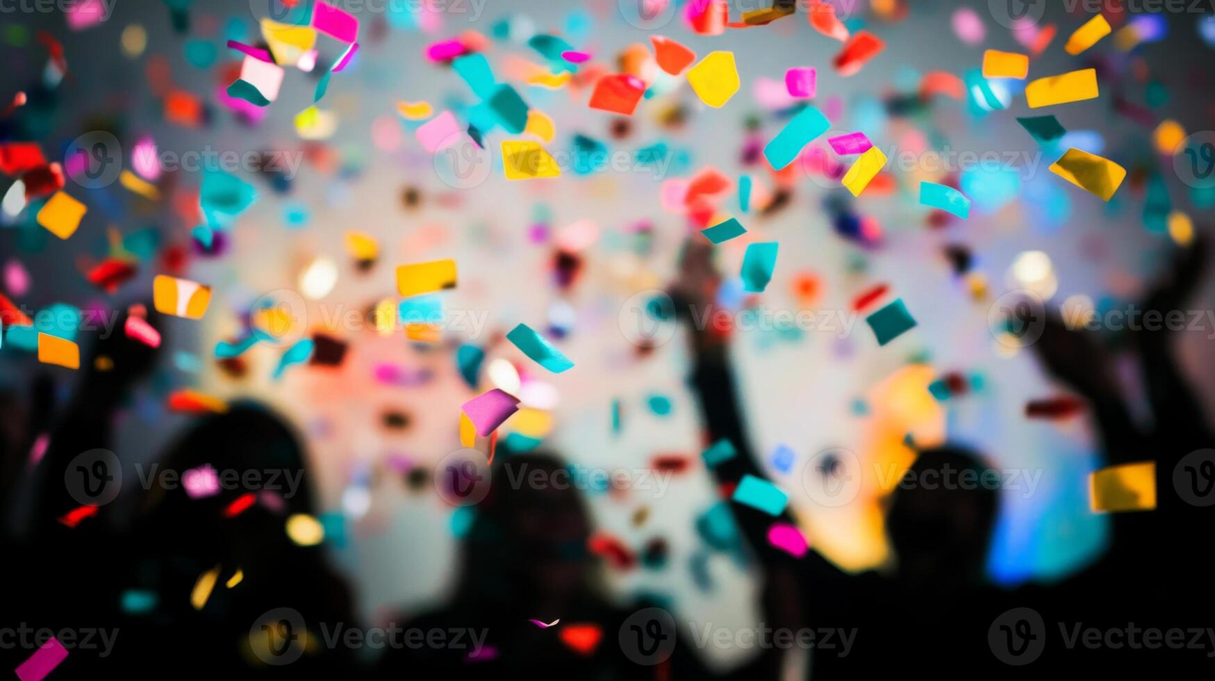 A close-up of falling confetti in focus, with blurred silhouettes of people celebrating in the background photo