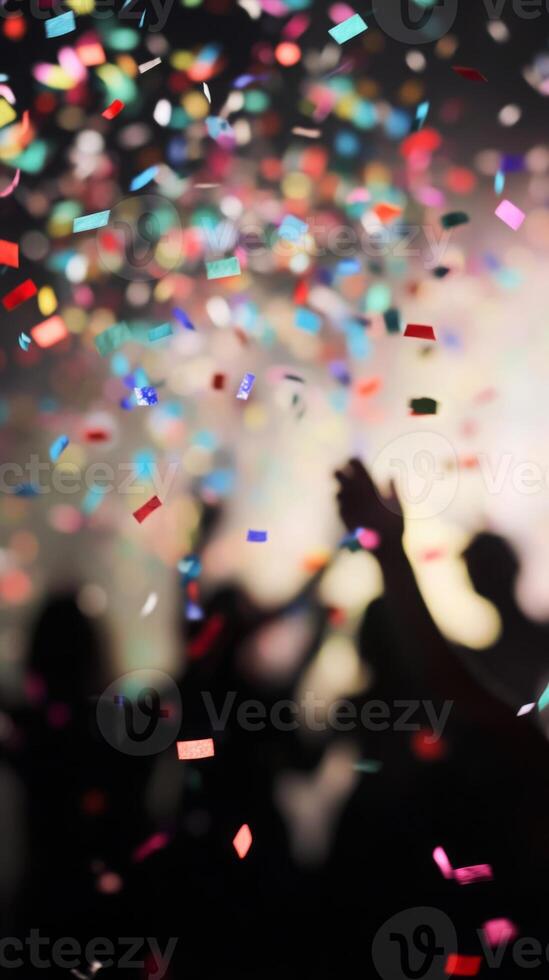 A close-up of falling confetti in focus, with blurred silhouettes of people celebrating in the background photo