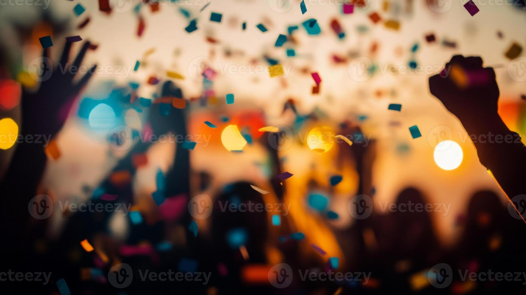 A close-up of falling confetti in focus, with blurred silhouettes of people celebrating in the background photo