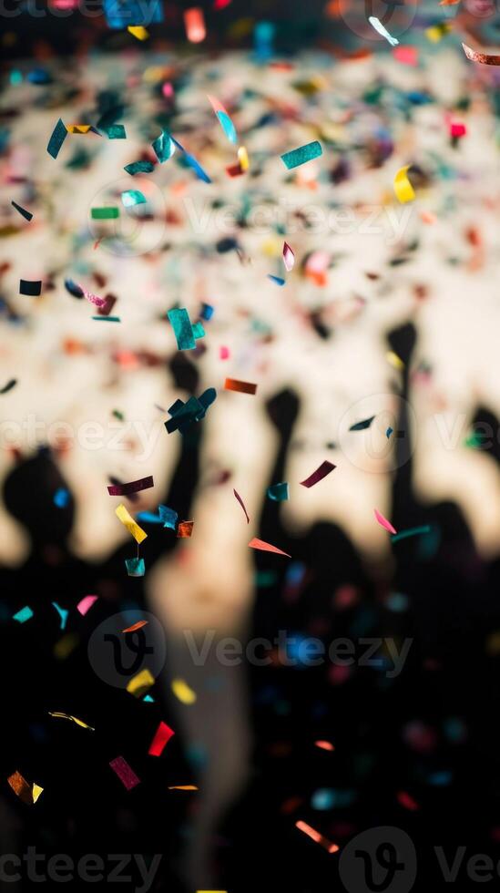 A close-up of falling confetti in focus, with blurred silhouettes of people celebrating in the background photo