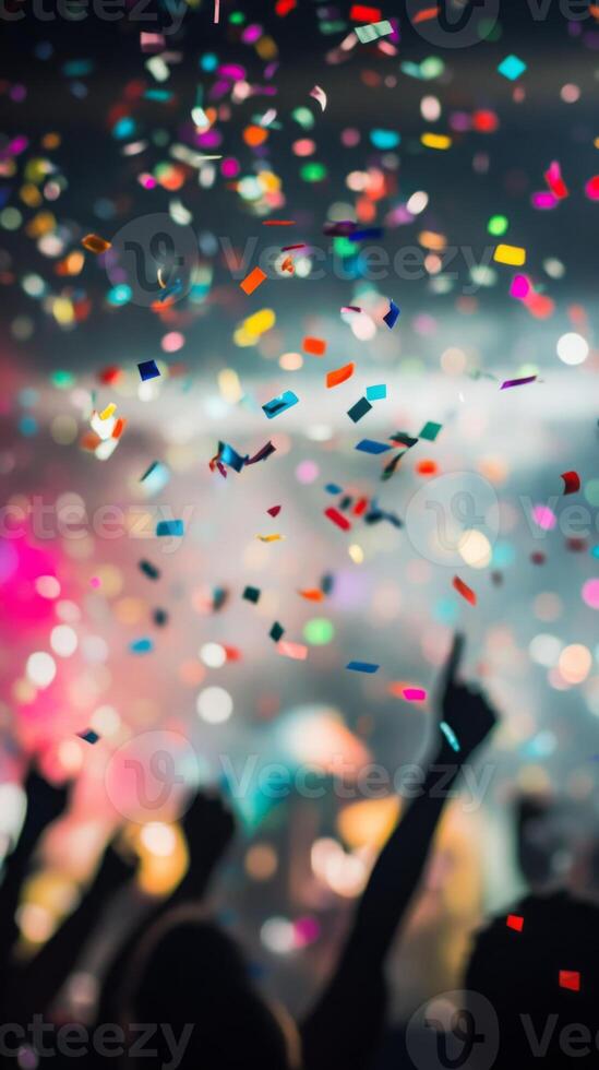 A close-up of falling confetti in focus, with blurred silhouettes of people celebrating in the background photo