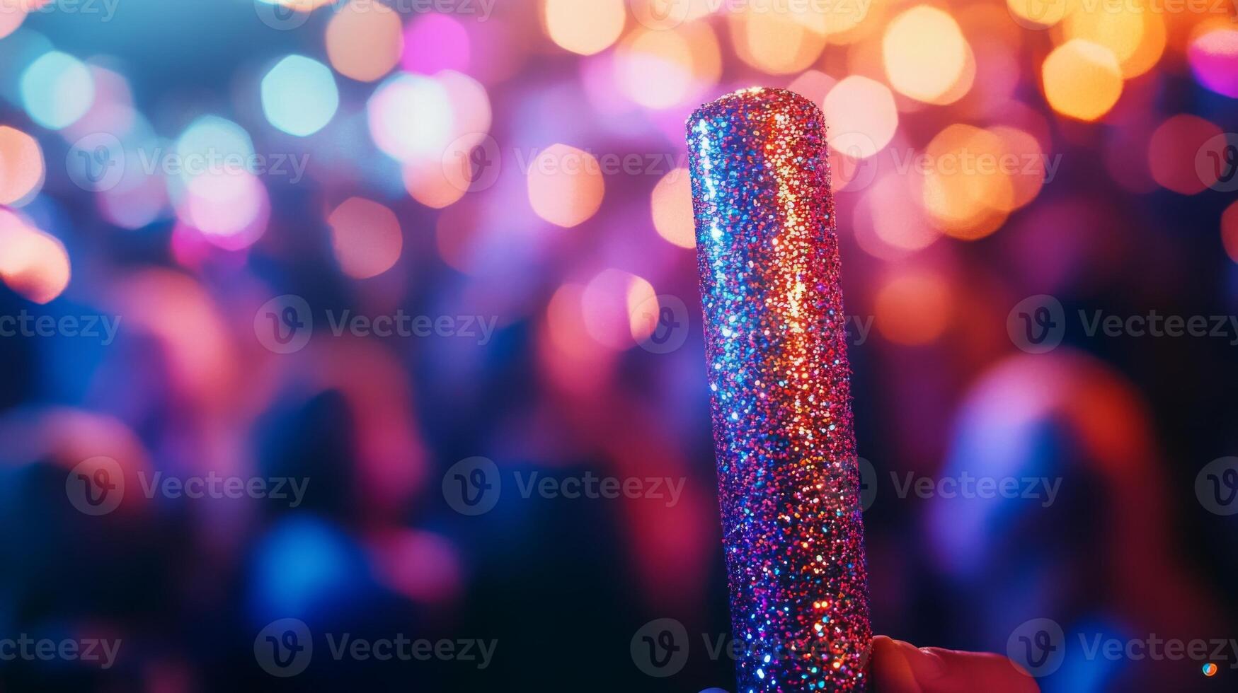 A glittery noisemaker, with a blurred crowd in the background photo