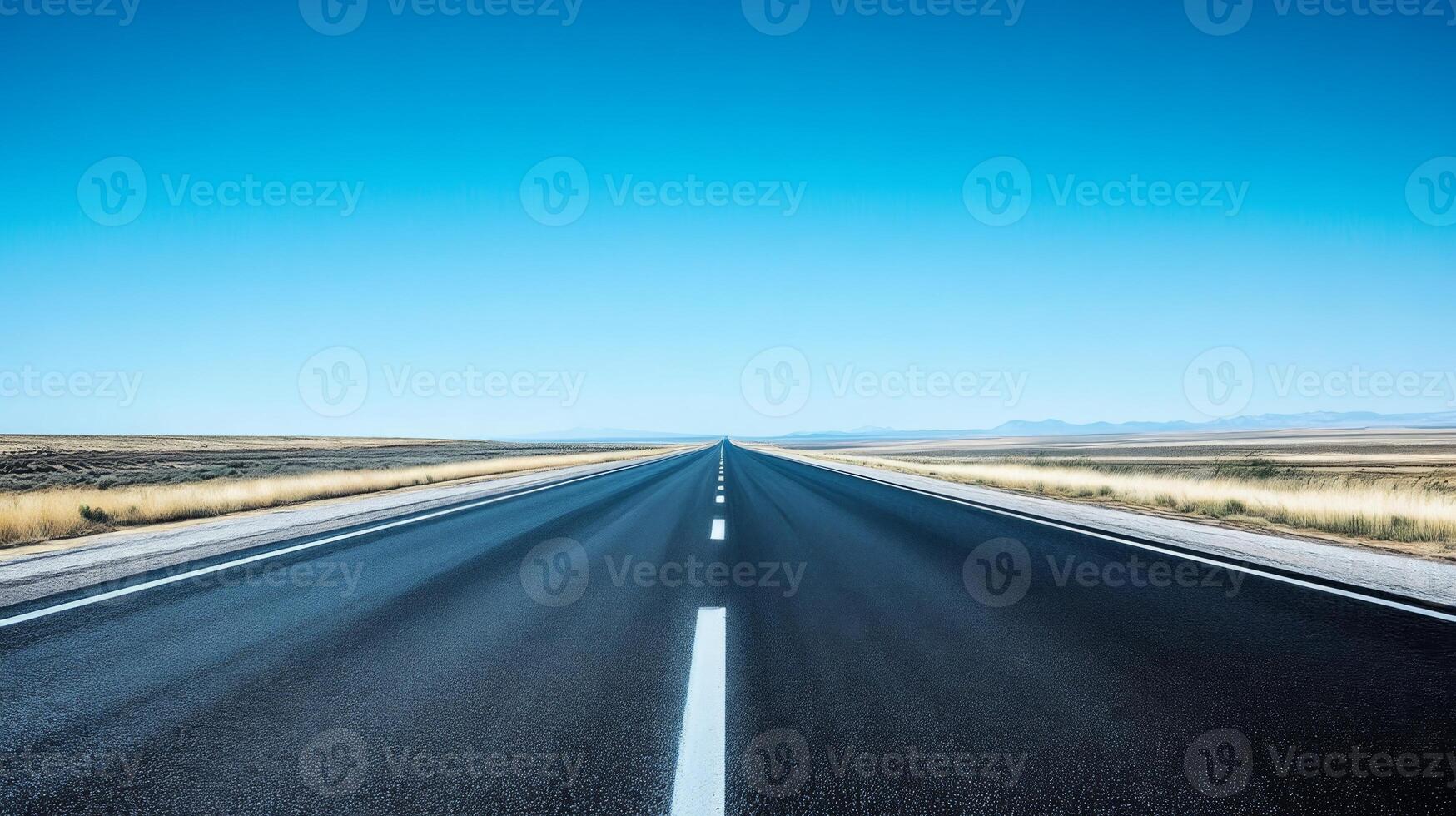 A wide-angle shot of an empty highway stretching into the horizon under a clear blue sky photo