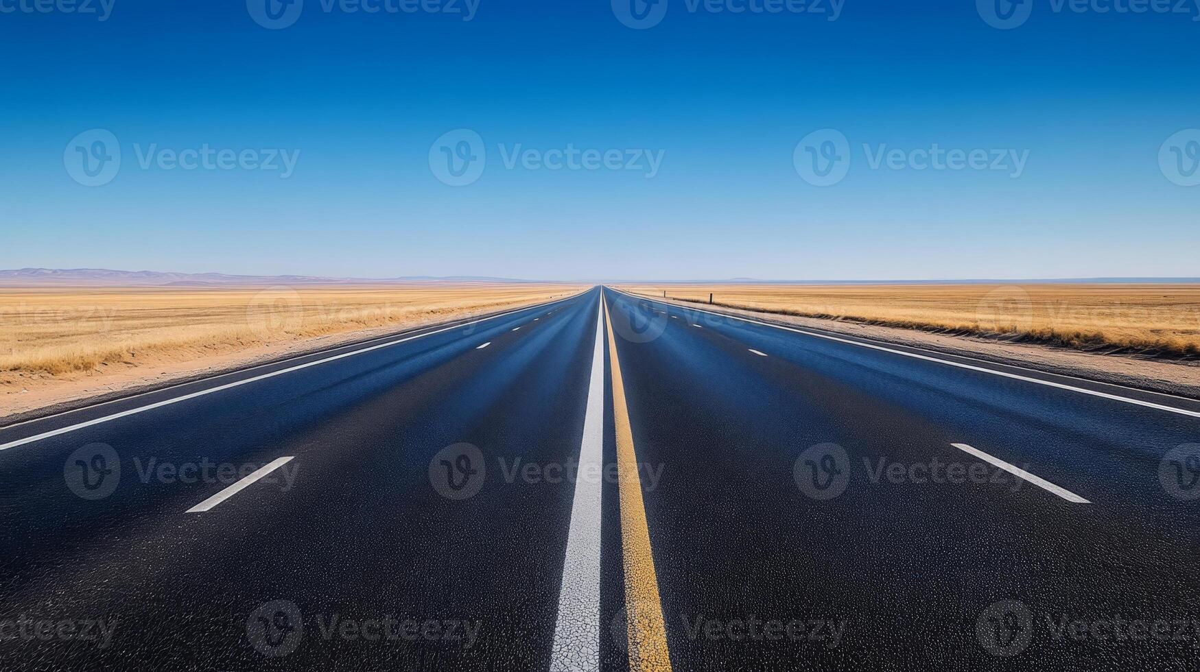 A wide-angle shot of an empty highway stretching into the horizon under a clear blue sky photo