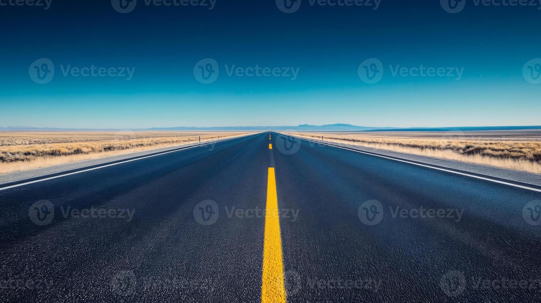 A wide-angle shot of an empty highway stretching into the horizon under a clear blue sky photo