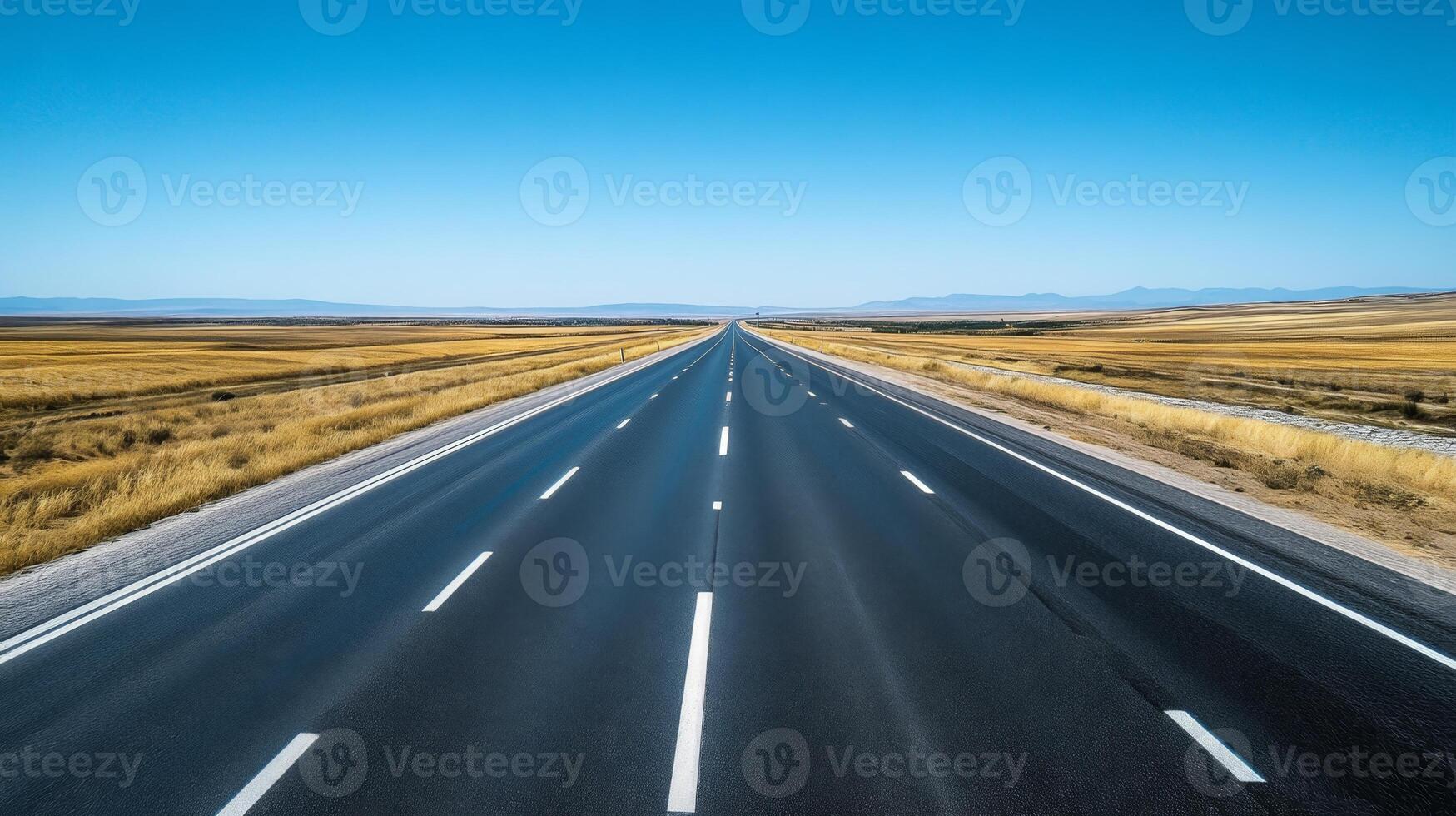 A wide-angle shot of an empty highway stretching into the horizon under a clear blue sky photo