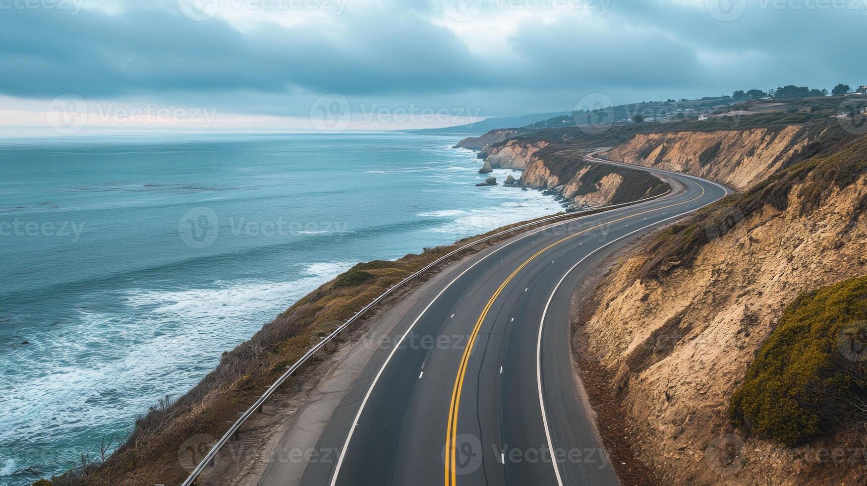 Empty coastal highway hugging the shoreline, with the ocean to one side and cliffs on the other photo