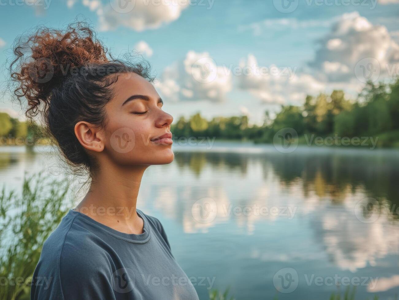 Woman enjoying a calm moment outdoors, standing by a peaceful lake with her eyes closed, taking in the serenity, with space for copy in the sky photo