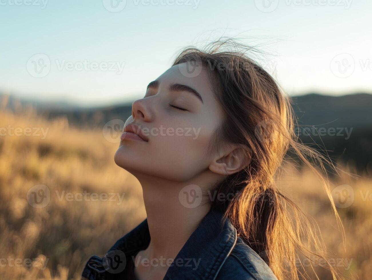 Young woman with her eyes closed, breathing in the fresh mountain air, standing at the edge of a field, with room for copy space in the background photo