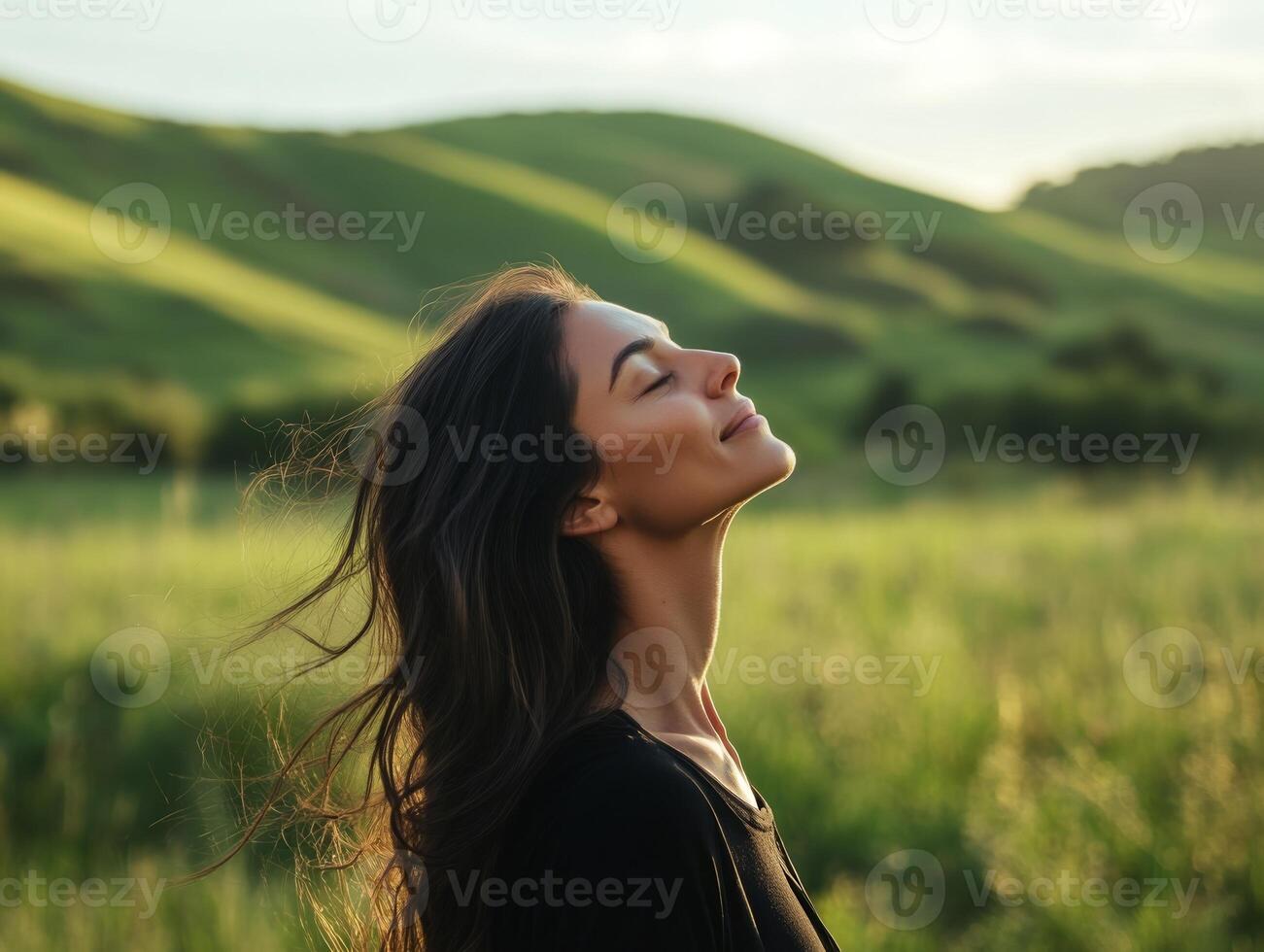A peaceful woman standing in a meadow, head tilted back, eyes shut, enjoying the calm breeze, with soft green hills in the background and copy space photo