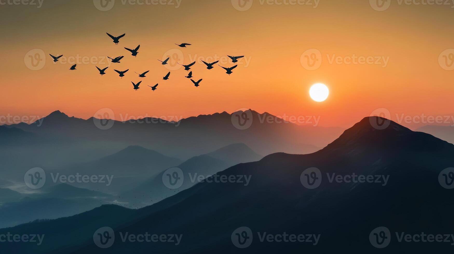 A flock of birds flying over a mountain range, silhouetted against the rising sun photo