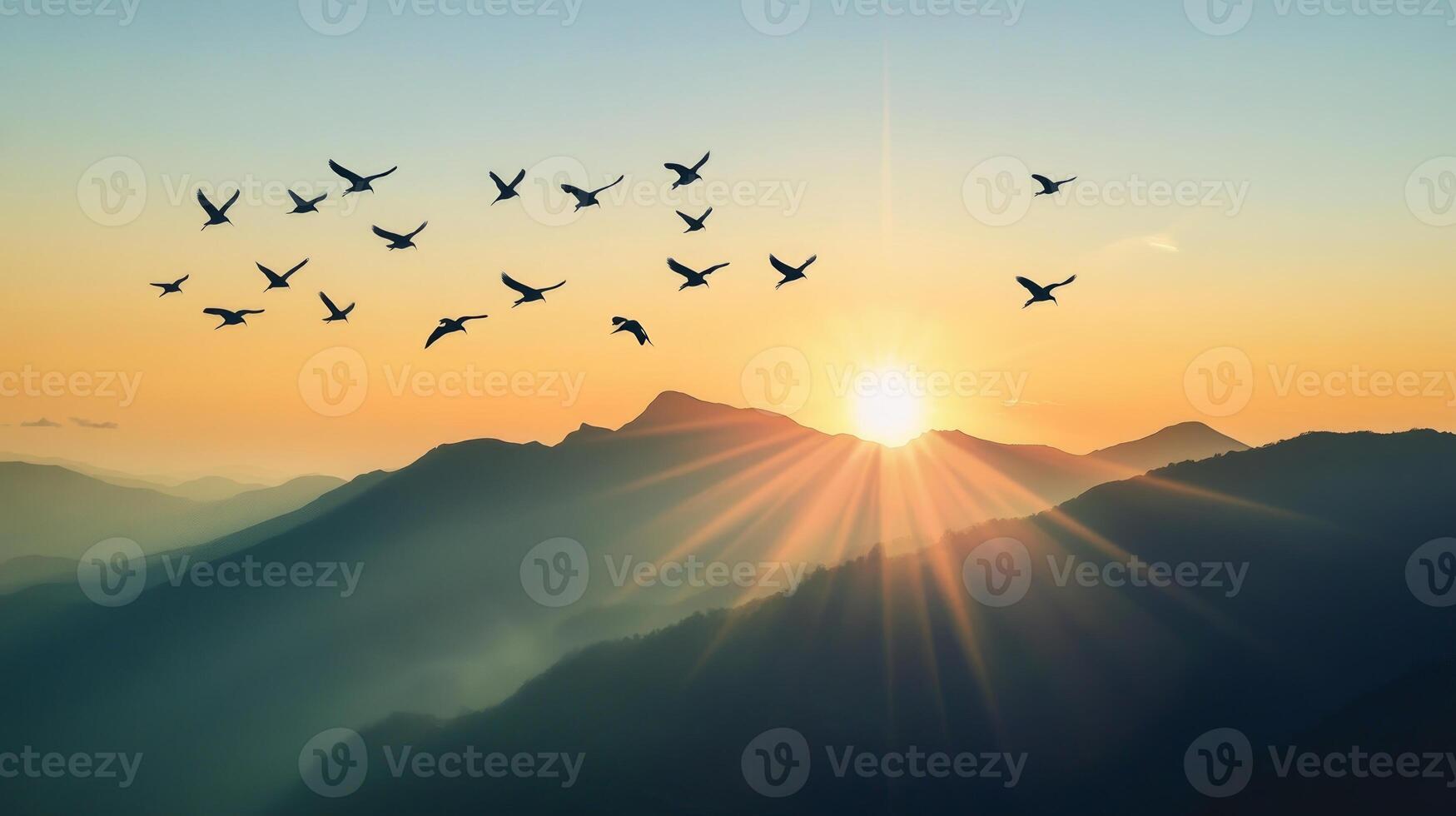 A flock of birds flying over a mountain range, silhouetted against the rising sun photo