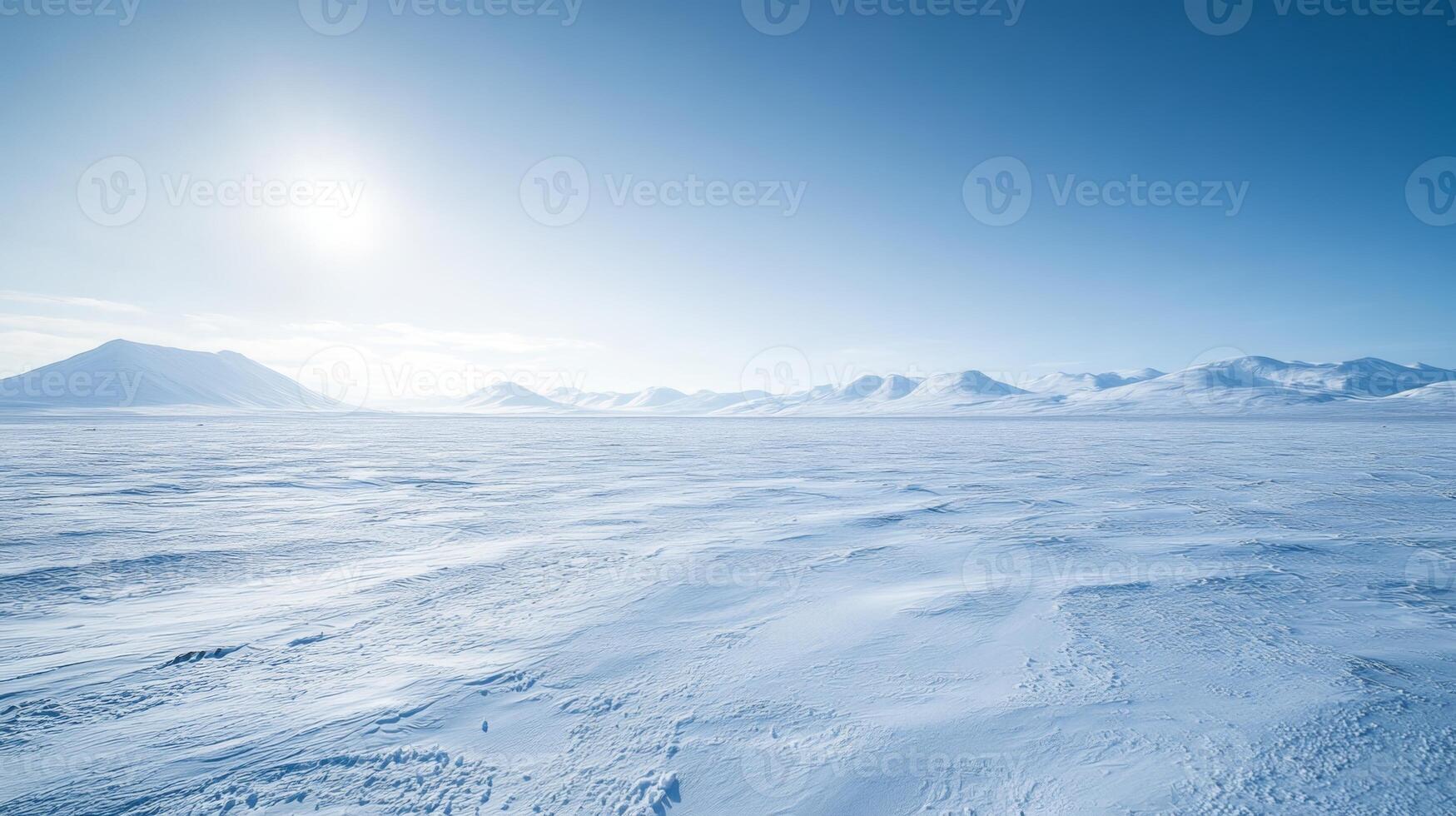 A wide, snow-covered plain stretching into the horizon, with distant mountains under a bright, cloudless winter sky photo