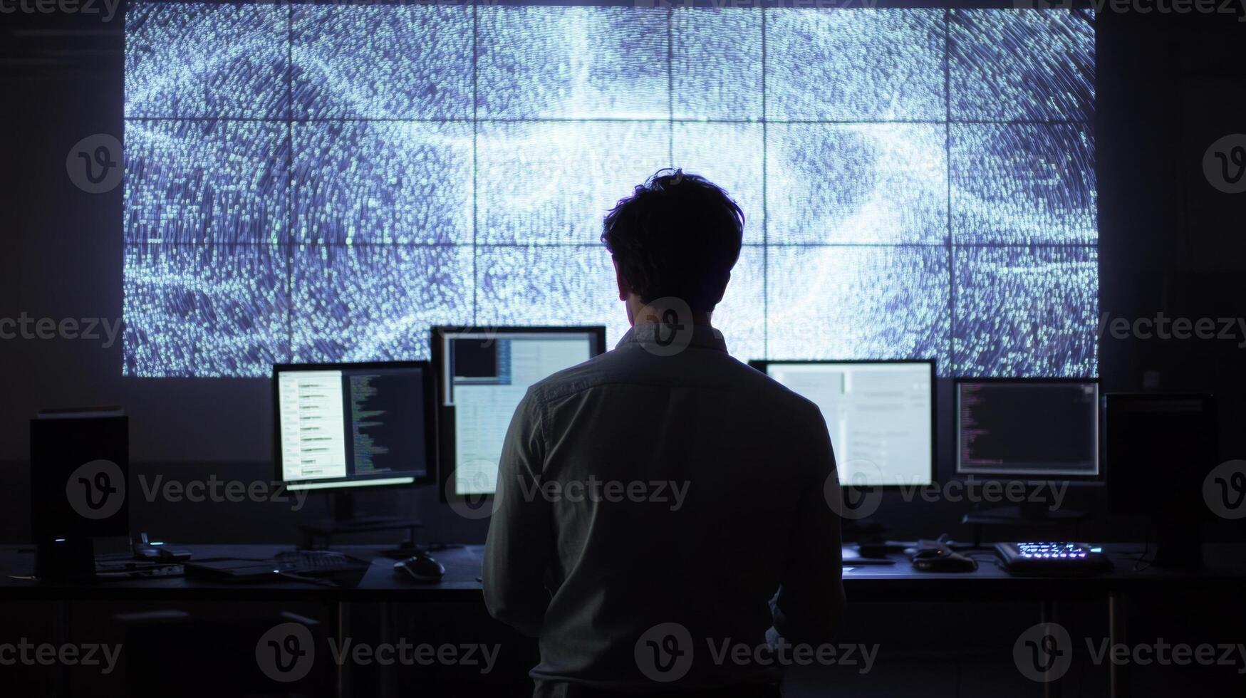 A man analyzing data on a large multi-screen setup in a dark room photo