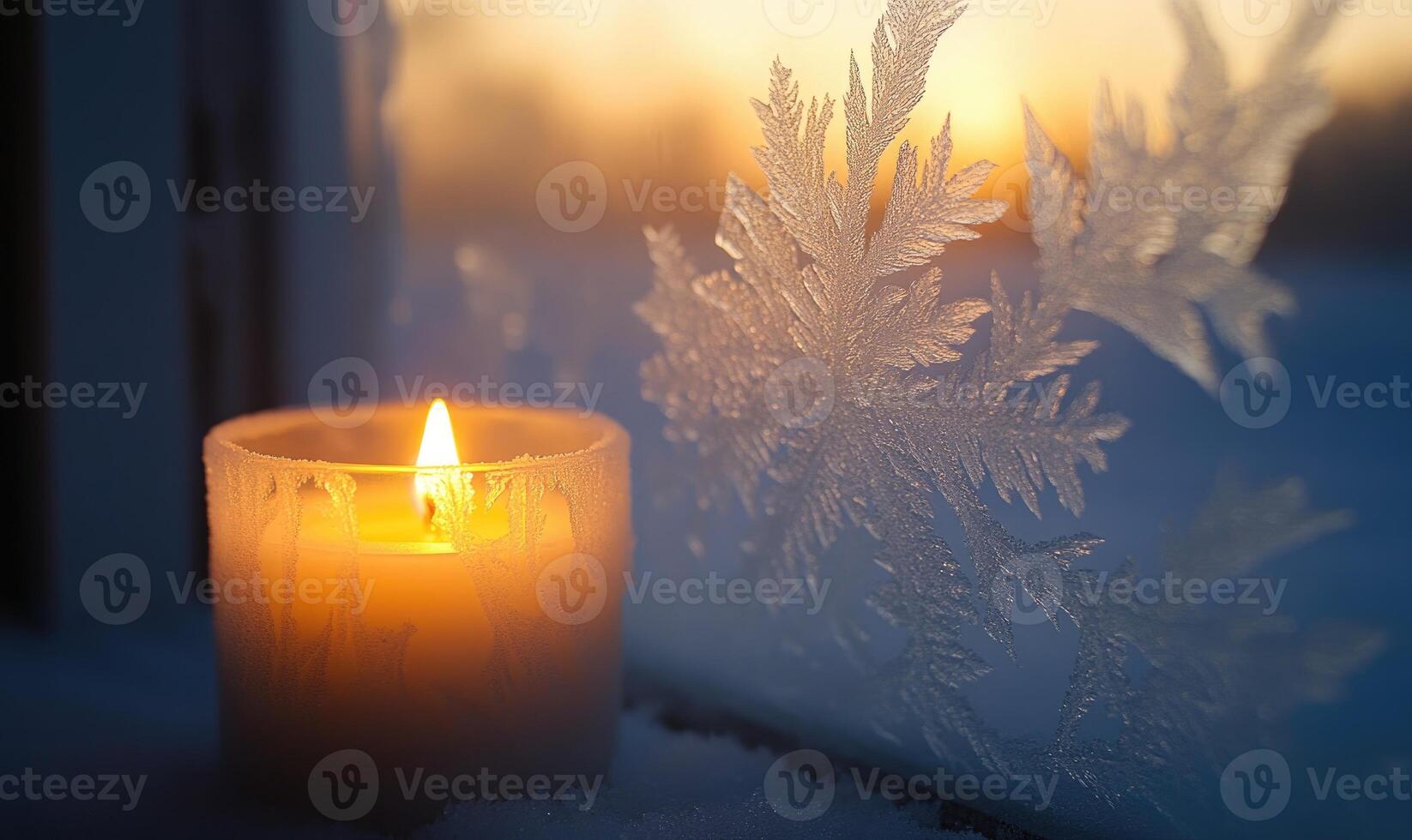 A candle is lit in front of a window with snowflakes on the glass photo