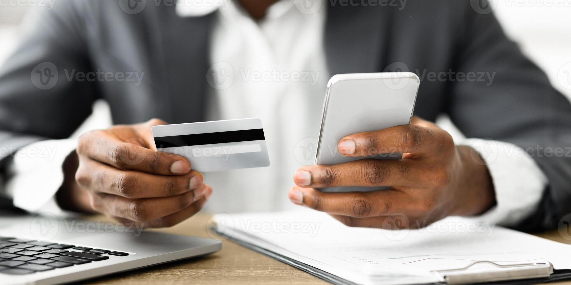 A person holds a credit card in their left hand and a smartphone in their right hand while looking at the screen. photo
