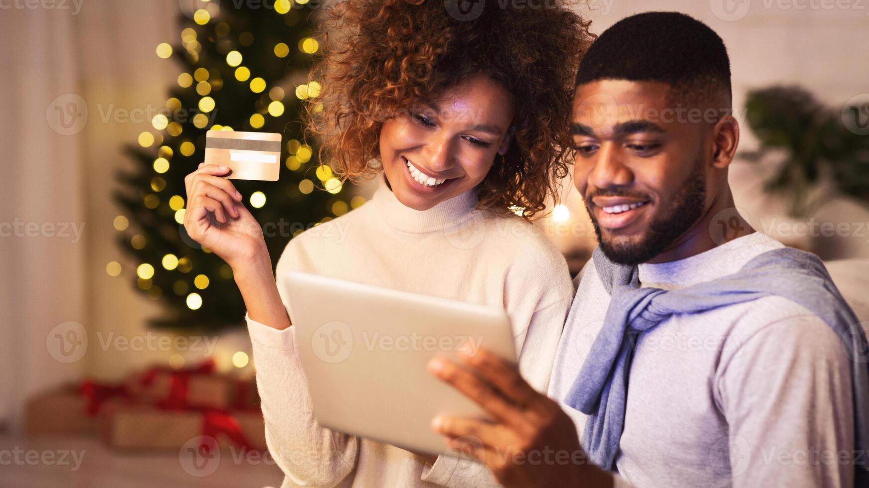 Christmas preparation. Happy black couple buying gifts online, using tablet and credit card photo
