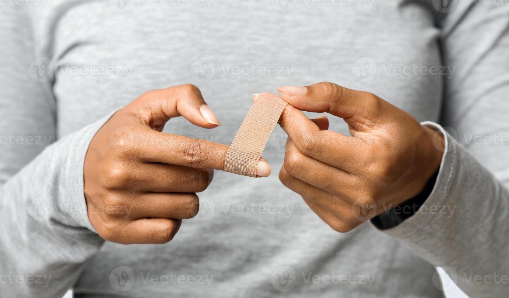 Black woman using adhesive tape on injured finger, self-treatment after trauma, close up photo