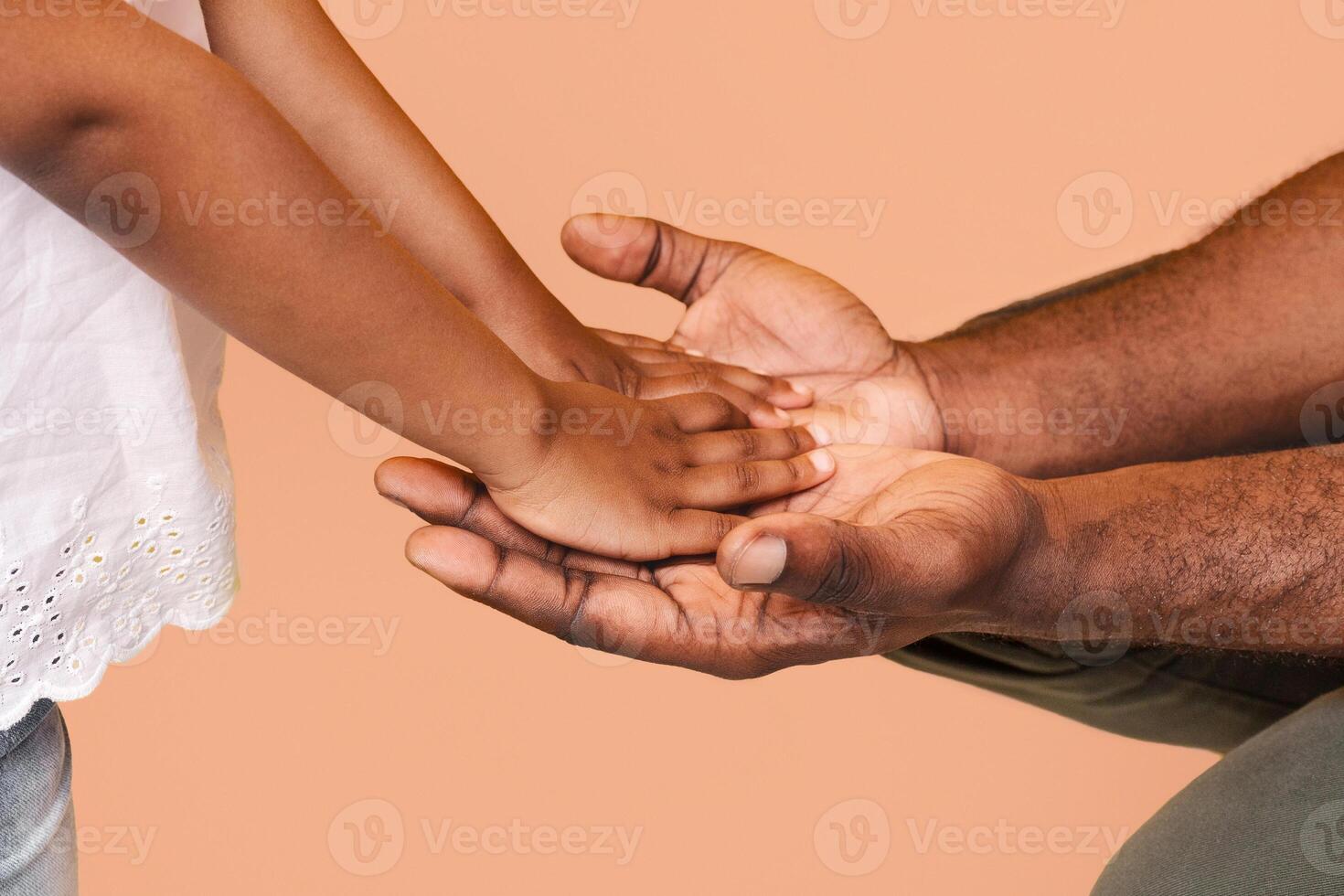 A close-up image captures the hands of an adult and a little child holding each other. The childs hand rests on top of the adults hand, with their fingers intertwined. photo