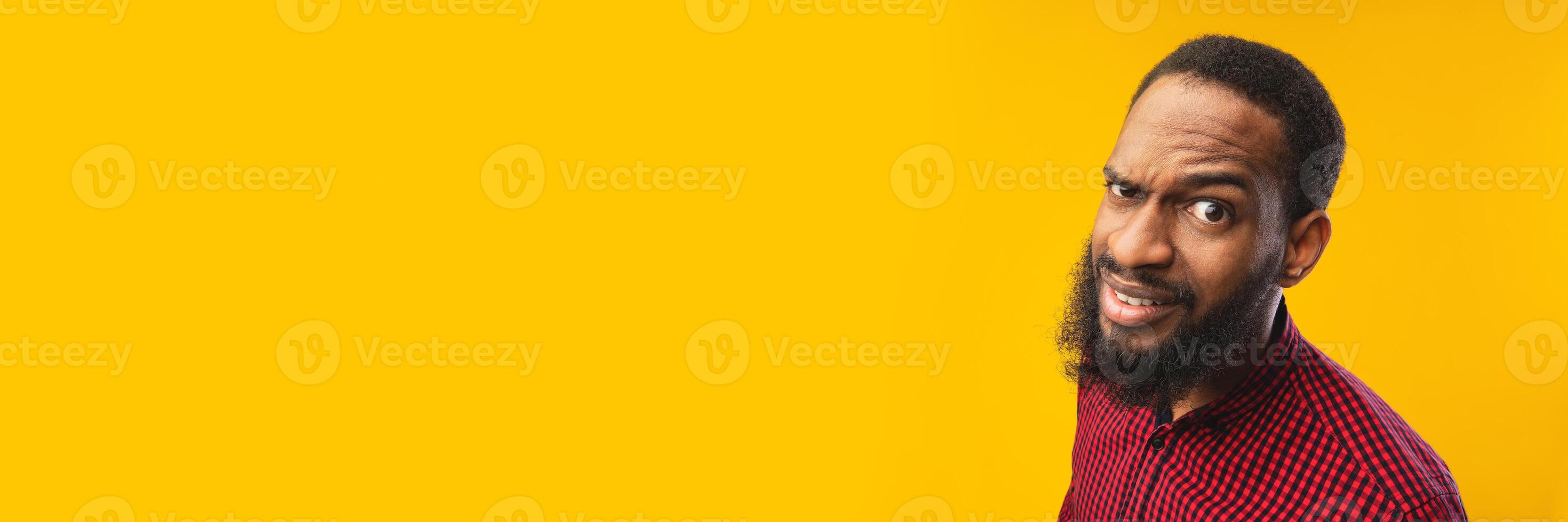Close up headshot of confused african american man looking at camera with raised eyebrow, yellow studio wall, panorama with copy space photo