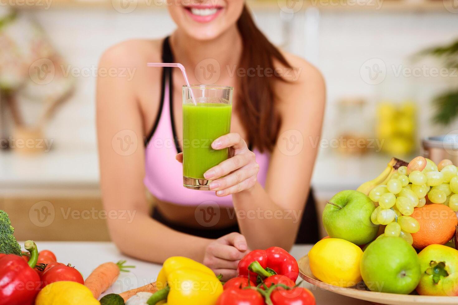 Happy Woman Drinking Fresh Green Detox Vegetable Juice, Showing Glass To Camera photo