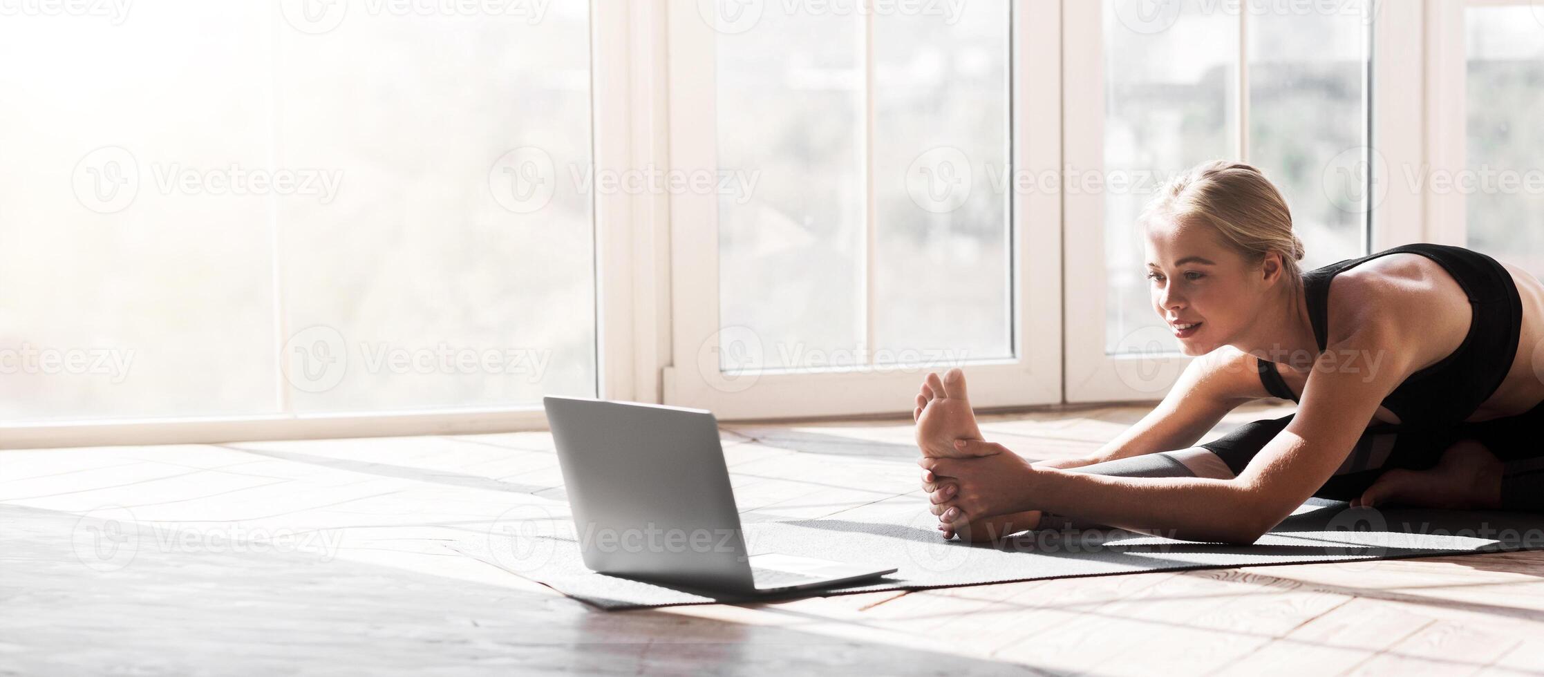 Sport application, website. Flexible young woman practicing yoga at home, using laptop, copy space photo