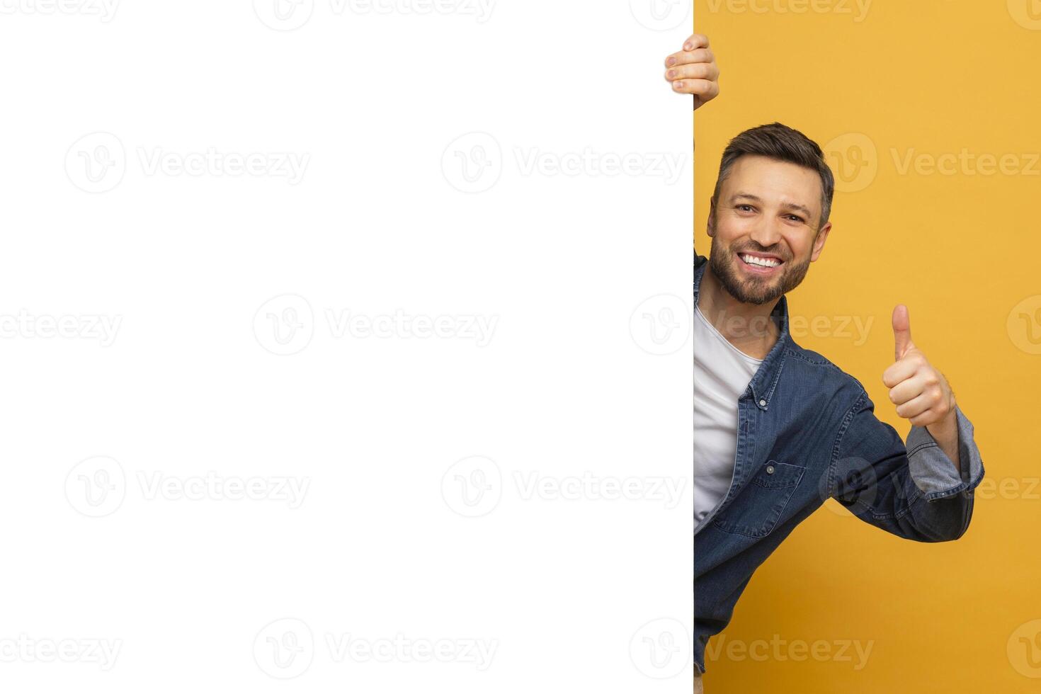 A man with a beard is standing and holding a sign in one hand while giving a thumbs up with the other hand. He appears to be expressing positivity or agreement. photo
